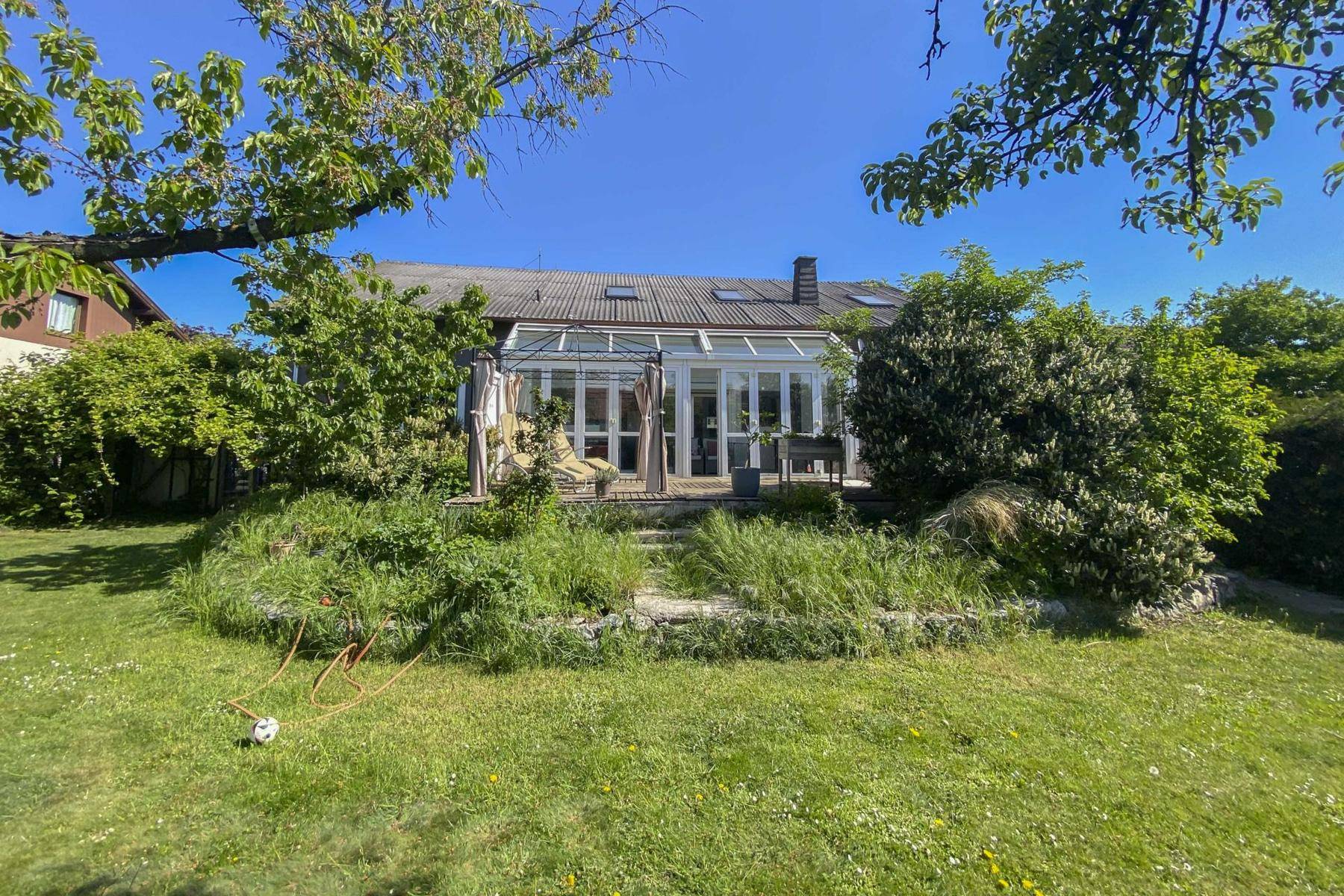 Rückansicht des Hauses mit Wintergarten und weitläufigem, gepflegtem Garten unter blauem Himmel.