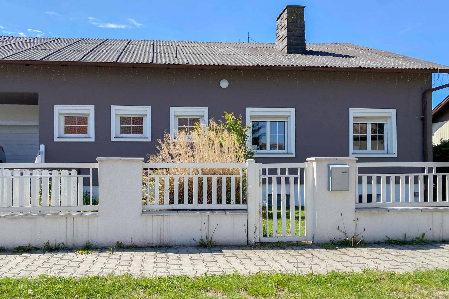 Graue Hausfassade mit weißen Fenstern und einem weißen Zaun, präsentiert einen gepflegten Eingangsbereich.