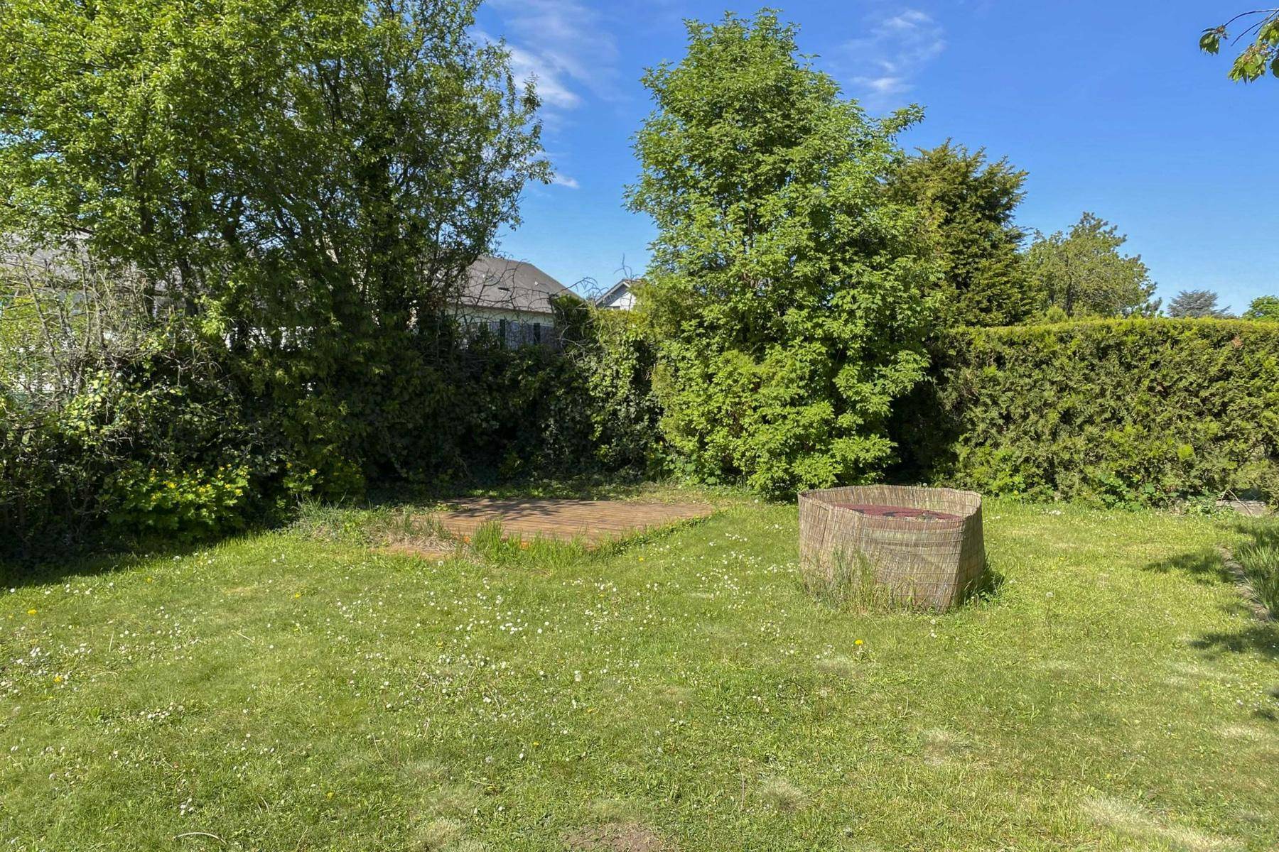 Weitläufiger Garten mit Rasenfläche, Bäumen und einem kleinen Holzpodest, bietet viel Platz im Freien.
