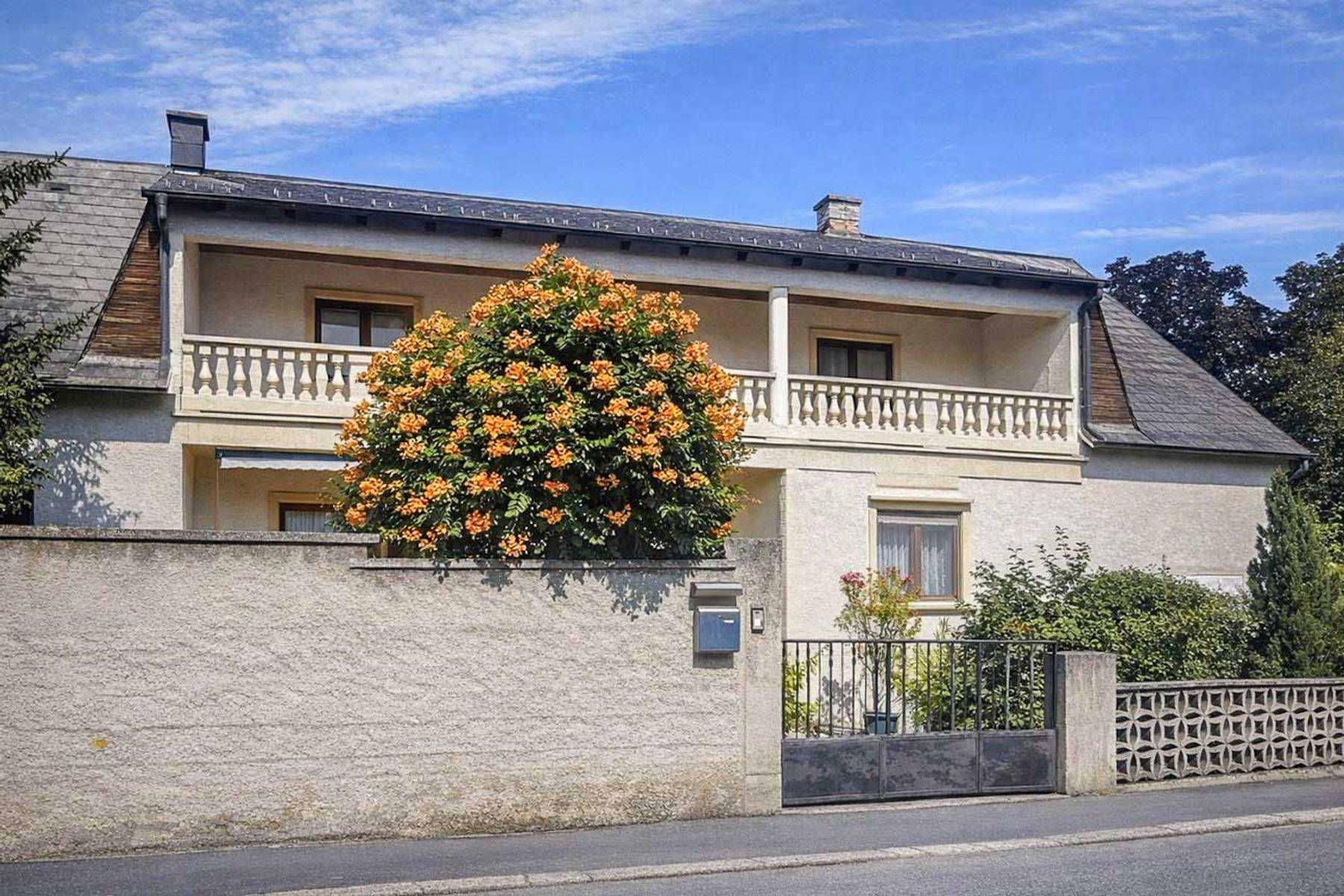 Charmantes Haus mit Balkon und blühendem Baum im Vorgarten.