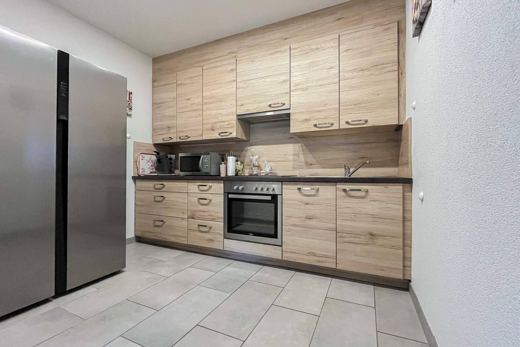 Funktionale Küche mit Holzoptik-Schränken, integrierten Geräten und Fliesenboden.