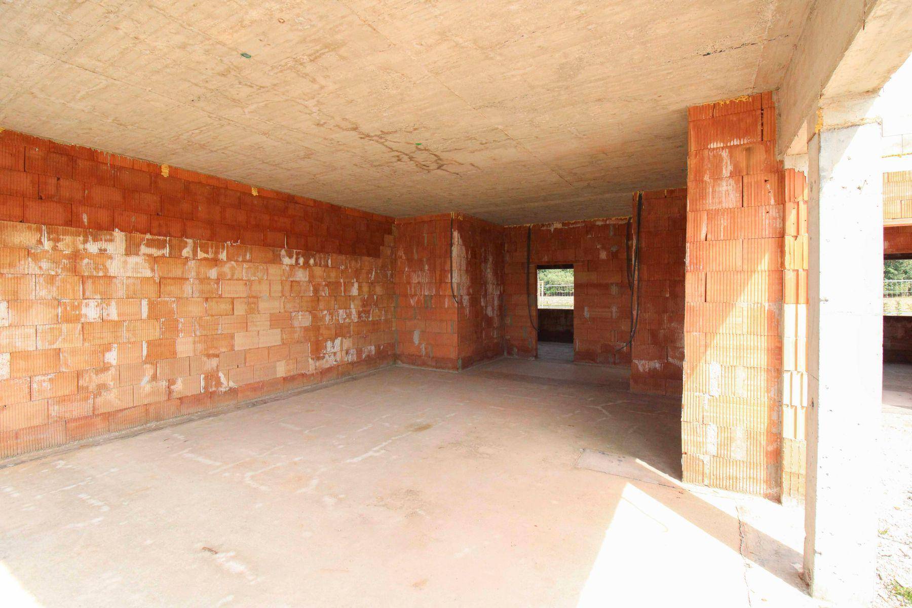 Großer Rohbauraum mit Ziegelwänden und Betonstützen, offen für zukünftige Gestaltung.
