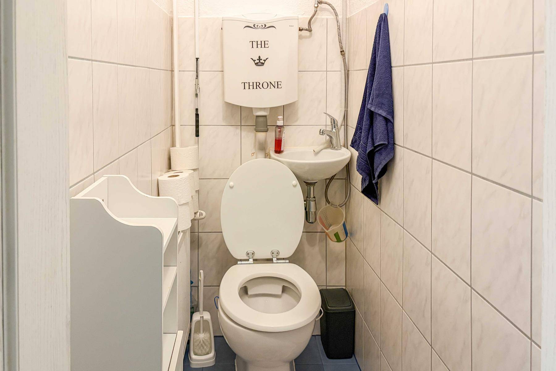 Kleines Gäste-WC mit weiß gefliesten Wänden, Toilette und einem kompakten Waschbecken.