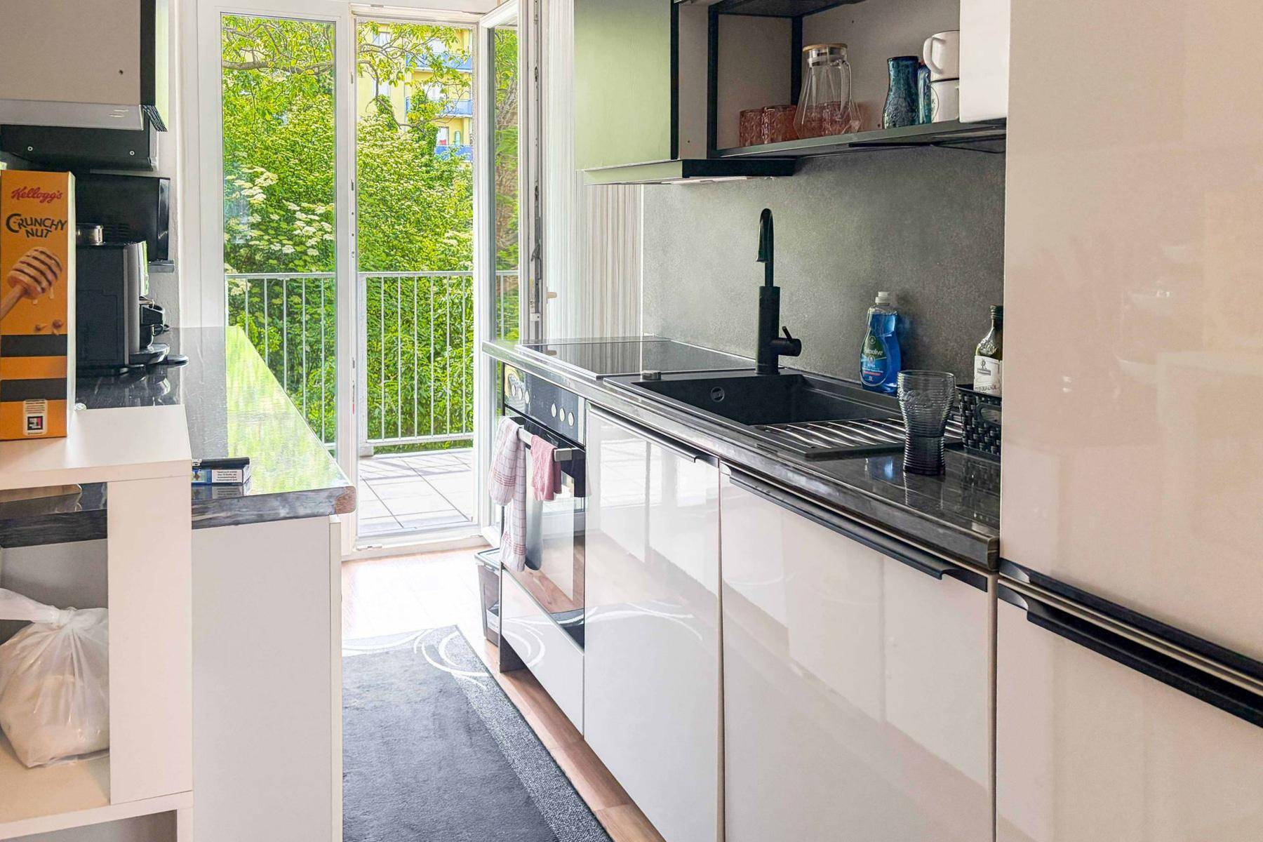 Küchenzeile mit Spüle, integriertem Backofen und direktem Zugang zum sonnigen Balkon mit viel Grün.