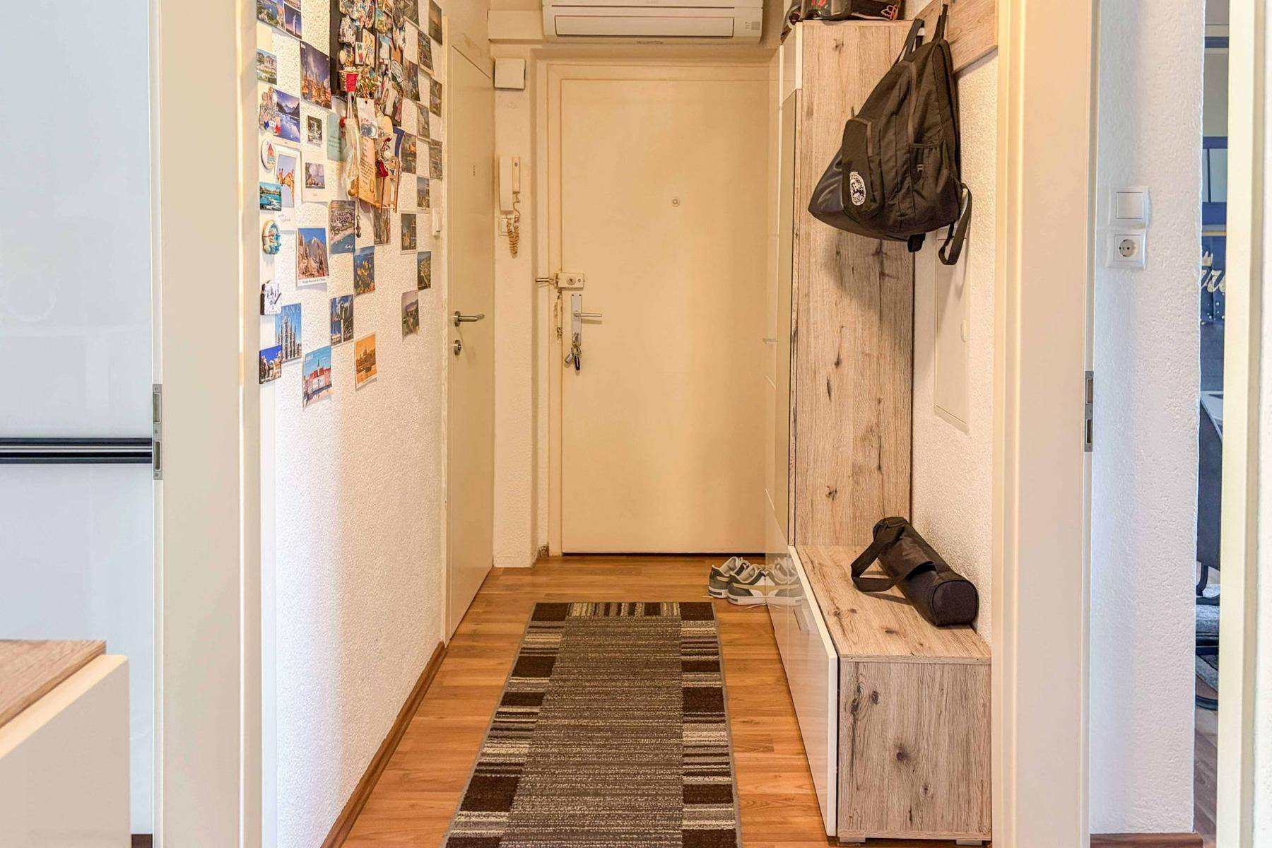 Eingangsbereich mit Laminatboden, Schuhbank und einer Wand, die mit vielen Fotos dekoriert ist.
