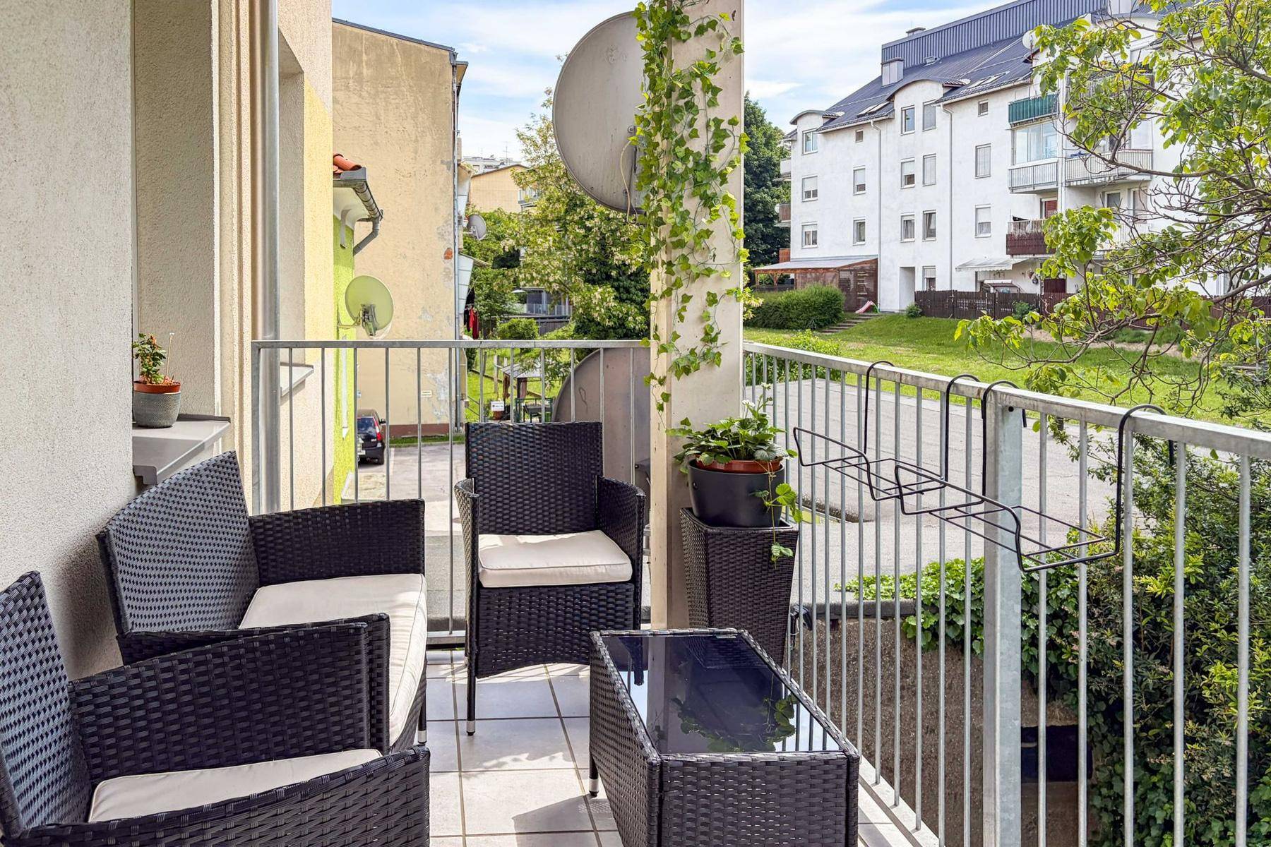 Gemütlicher Balkon mit Rattanmöbeln und Blick auf die umliegenden Gebäude und Grünflächen.