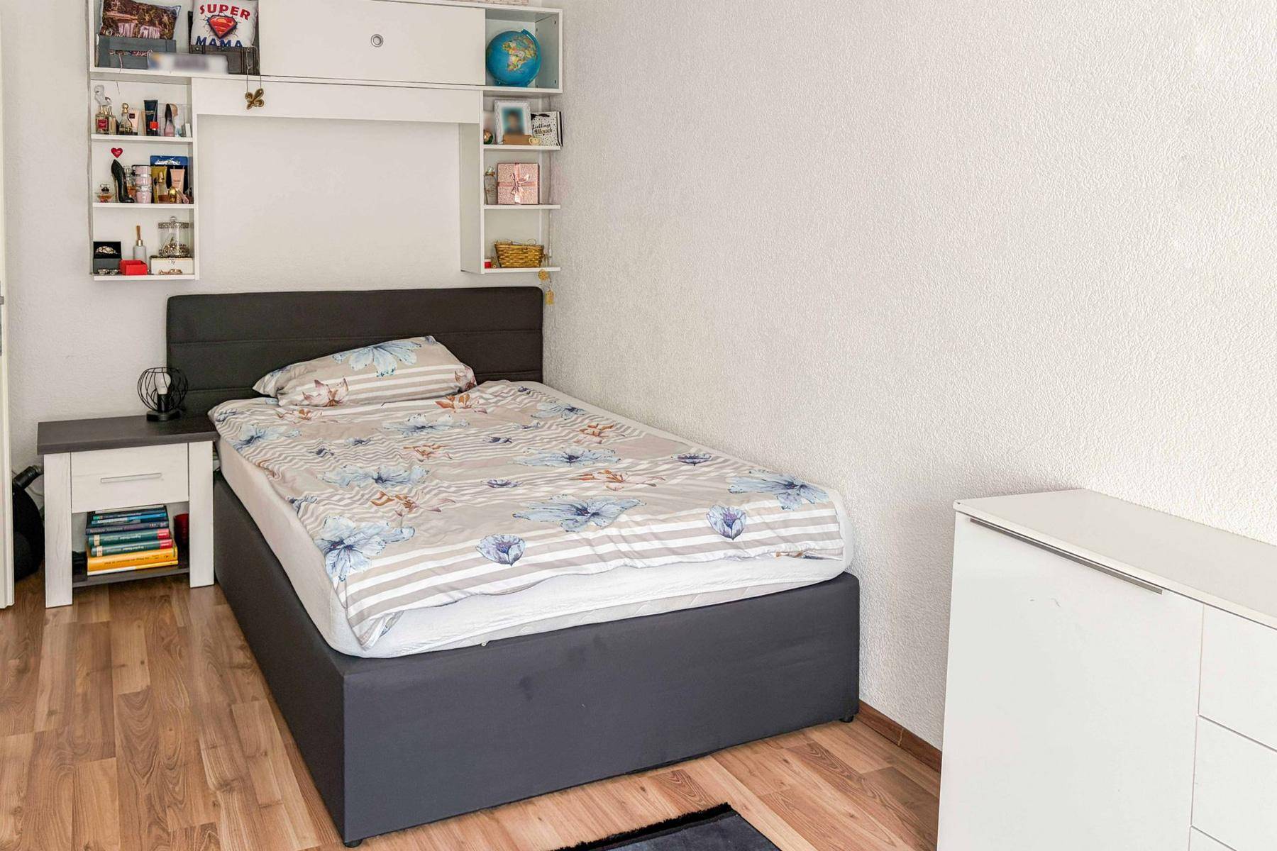 Schlafzimmer mit Einzelbett, Laminatboden und praktischen Wandregalen für Stauraum.