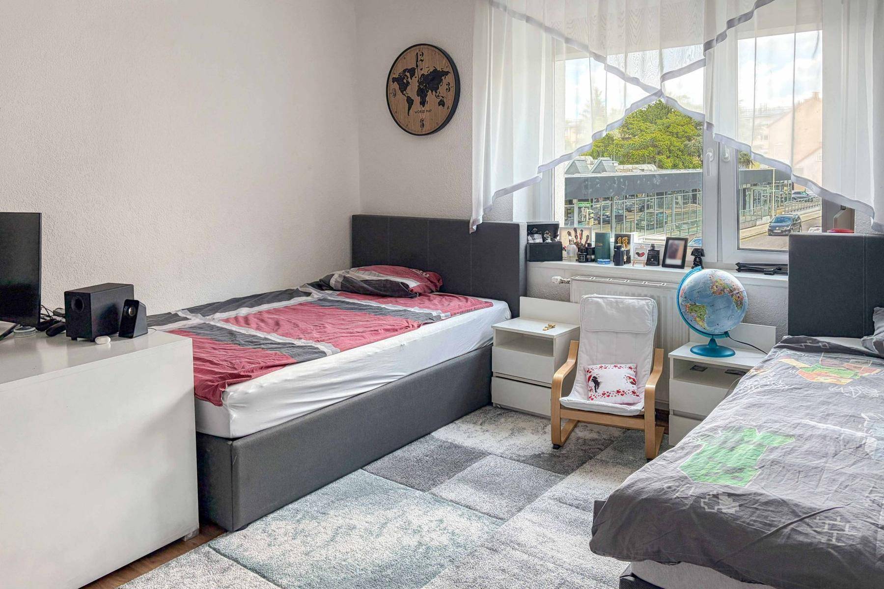 Kinderzimmer mit zwei Einzelbetten, Teppichboden und einem Fenster mit Blick auf die Straße.