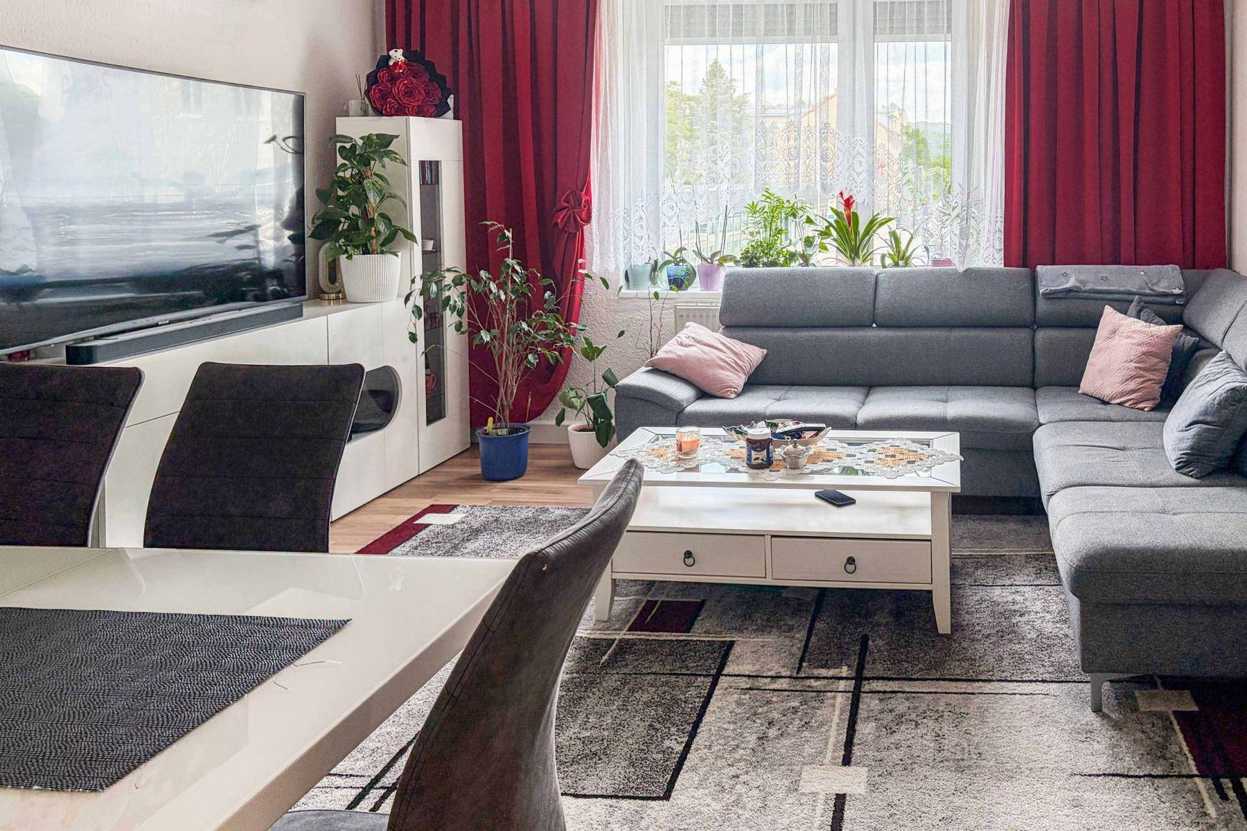 Offener Wohn-Essbereich mit großem Sofa, Esstisch und Fernseher, dekoriert mit roten Vorhängen.