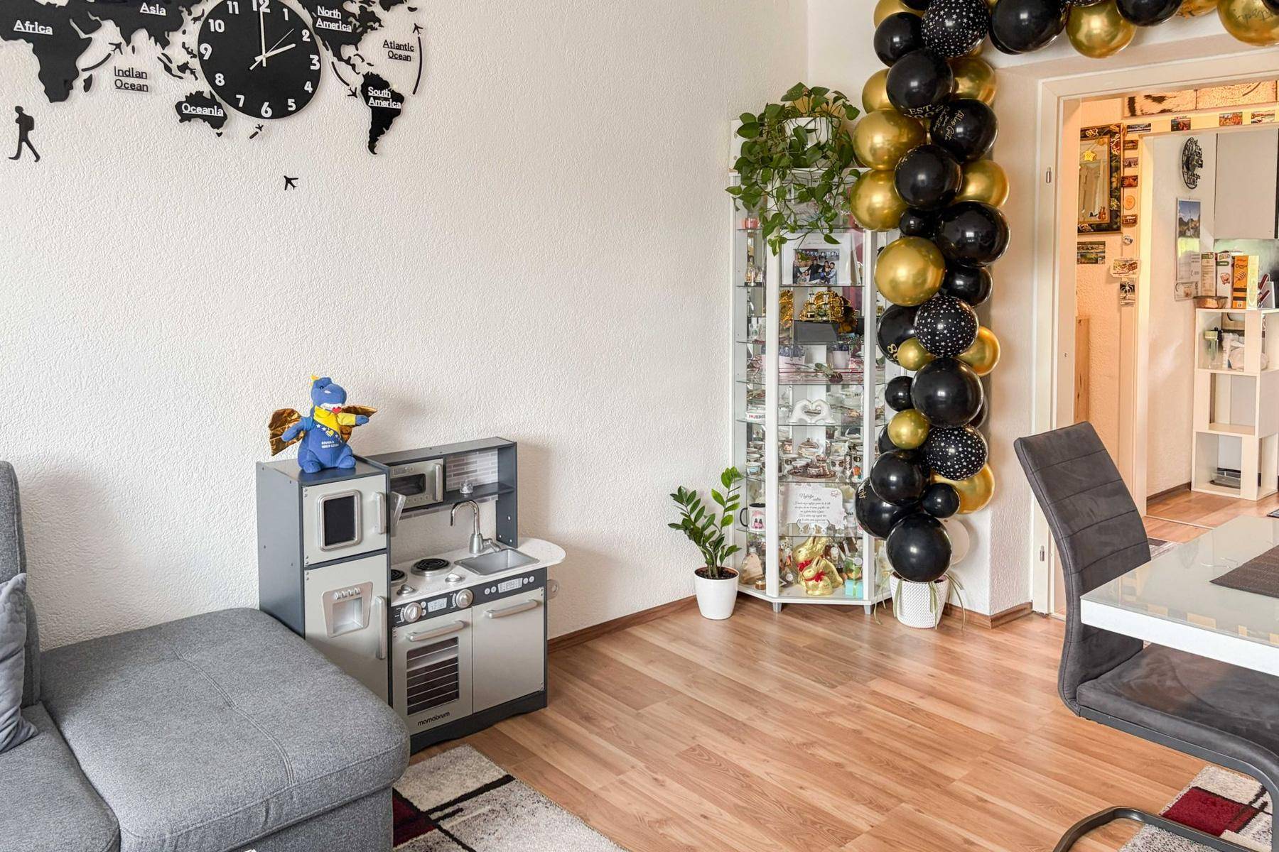 Heller Wohnbereich mit Kinderspielküche, dekorativer Ballongirlande und Laminatboden.