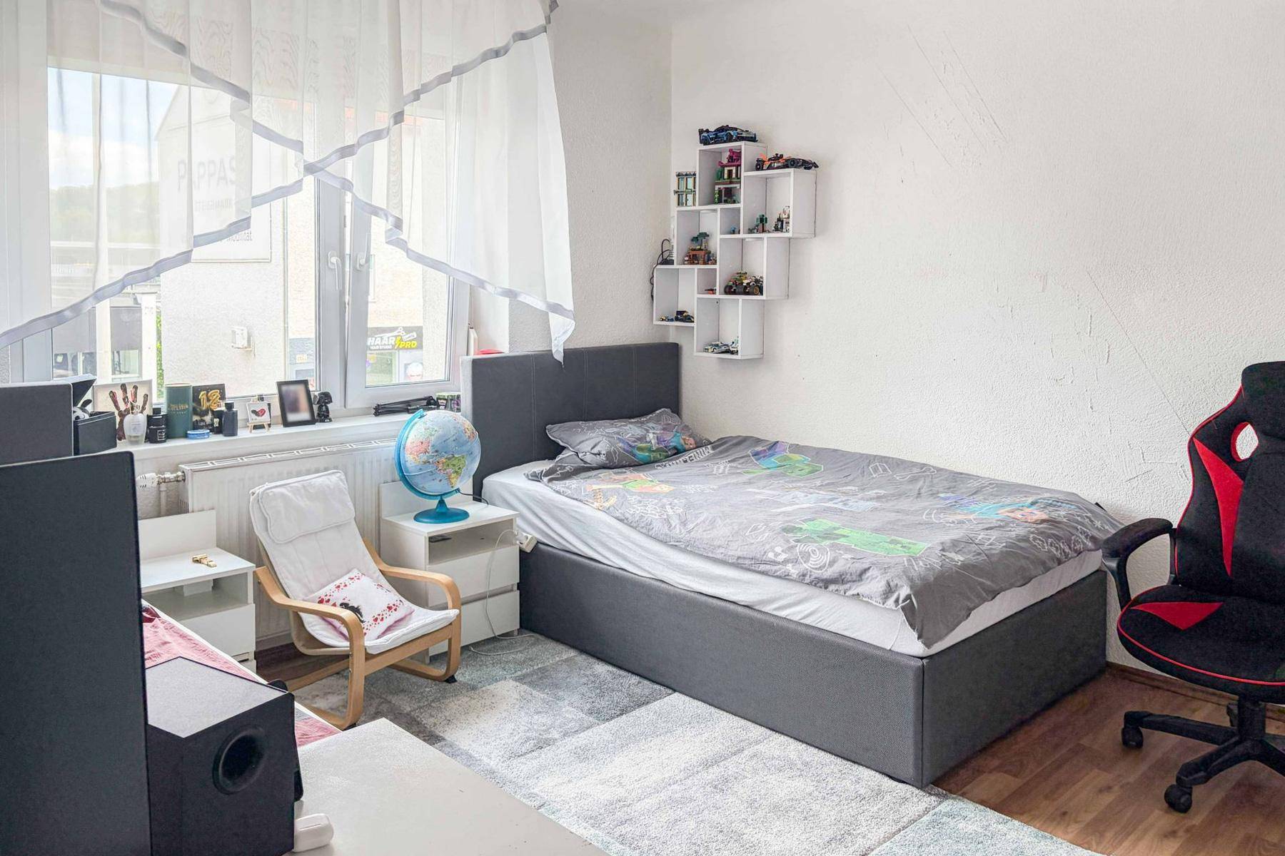 Jugendzimmer mit Einzelbett, Gaming-Stuhl und einem Fenster, das viel Tageslicht hereinlässt.