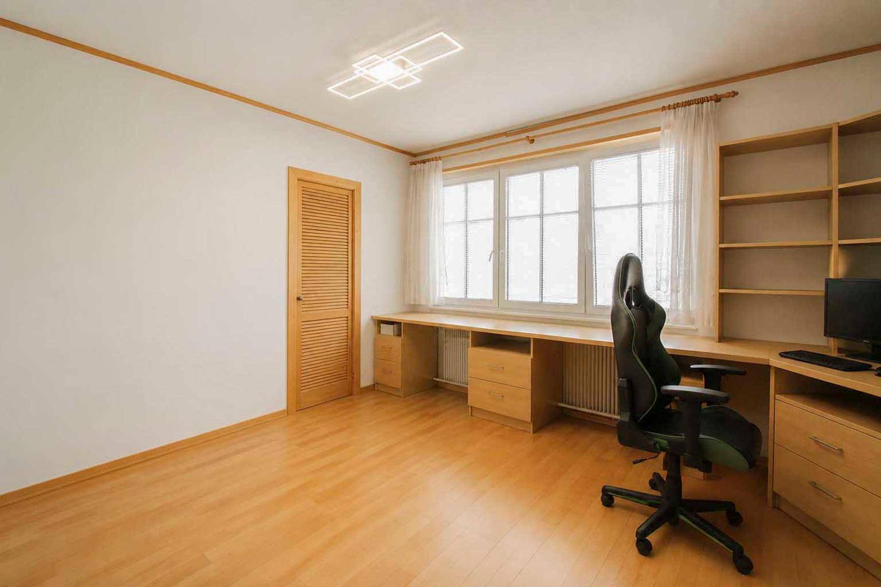 Helles Arbeitszimmer mit großem Schreibtisch, Regalen und Parkettboden.