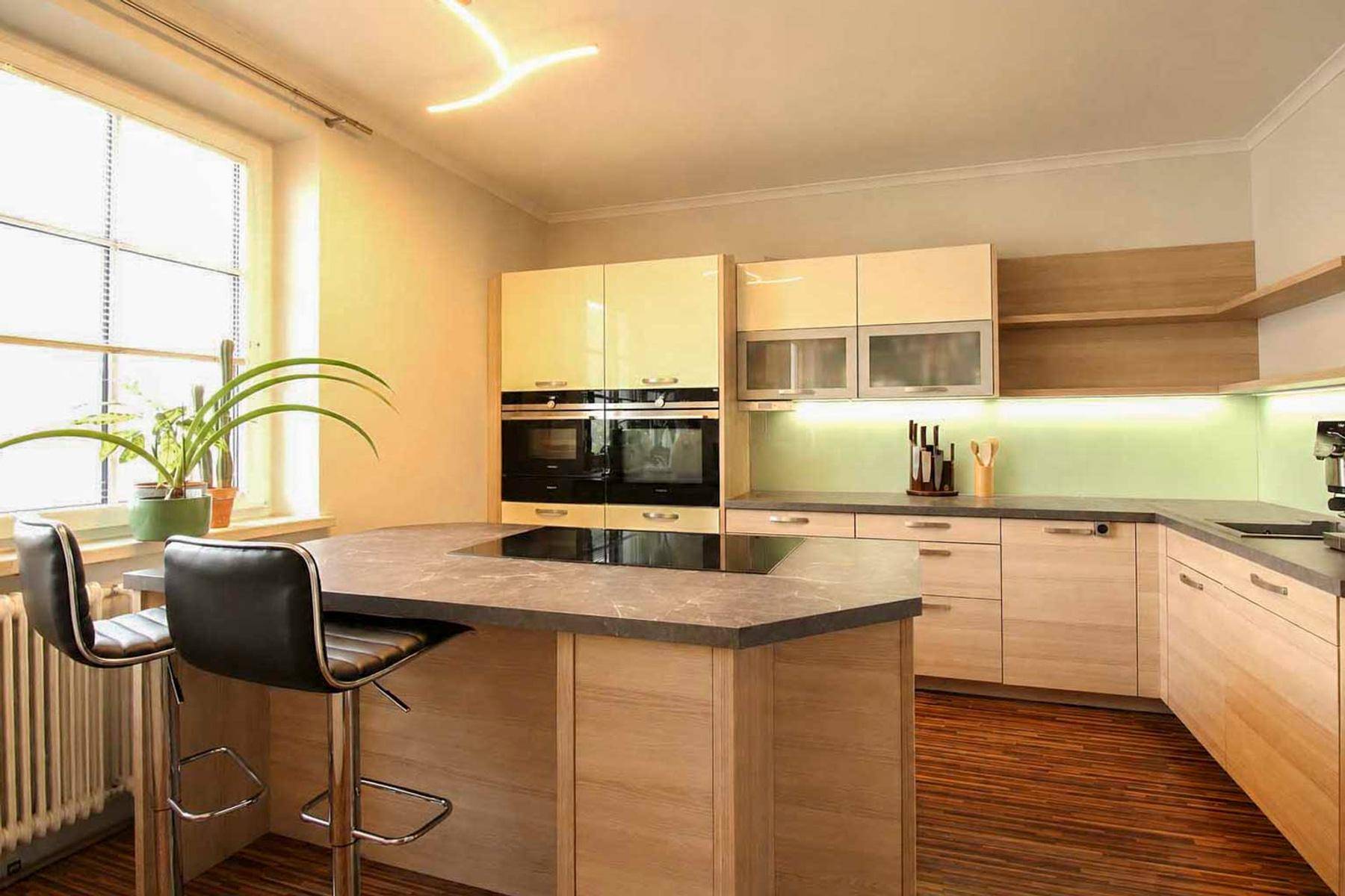 Moderne Küche mit heller Holzoptik, Kochinsel und integrierten Backöfen.