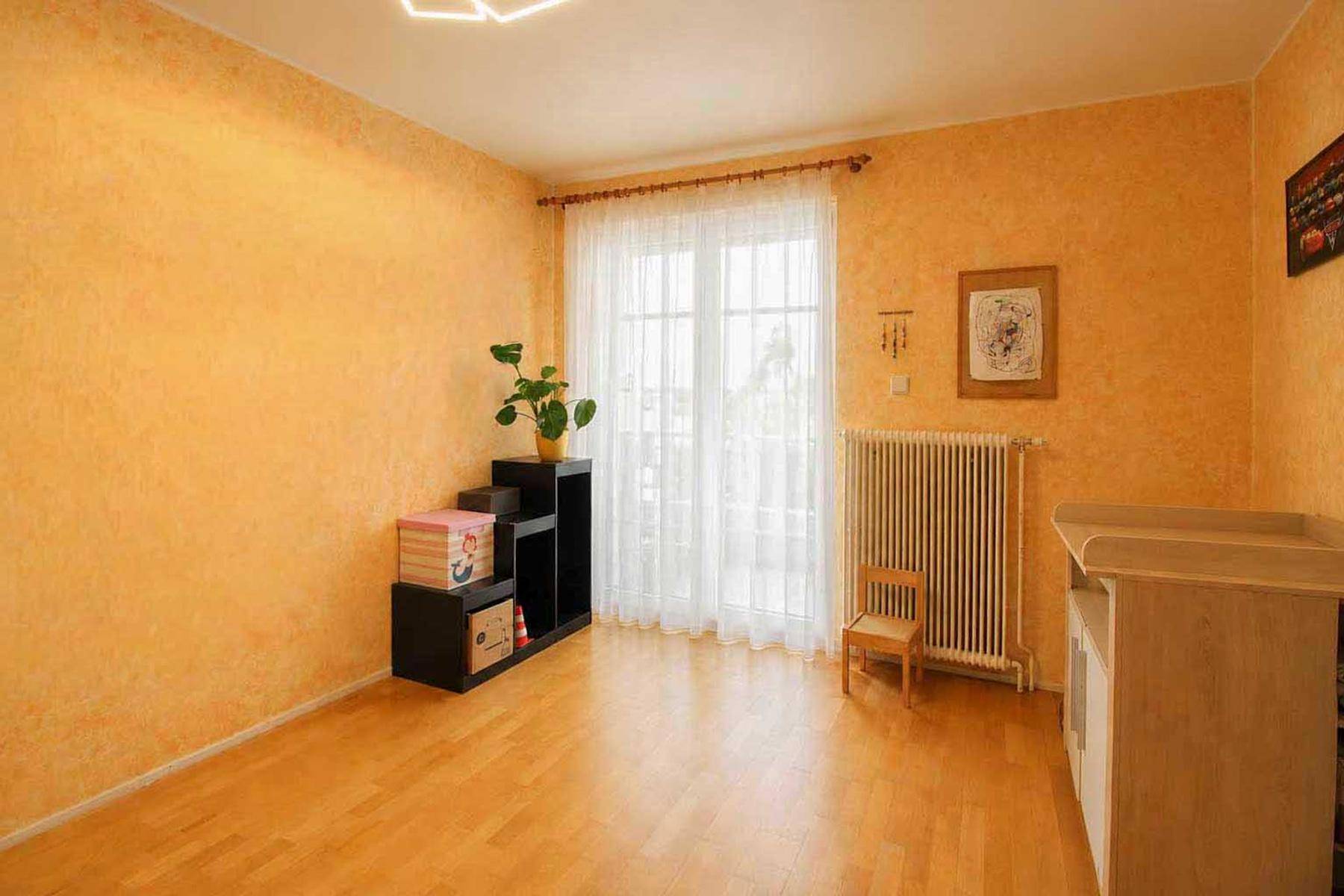Kinderzimmer mit hellem Parkettboden, farbiger Wandgestaltung und Zugang zum Balkon.
