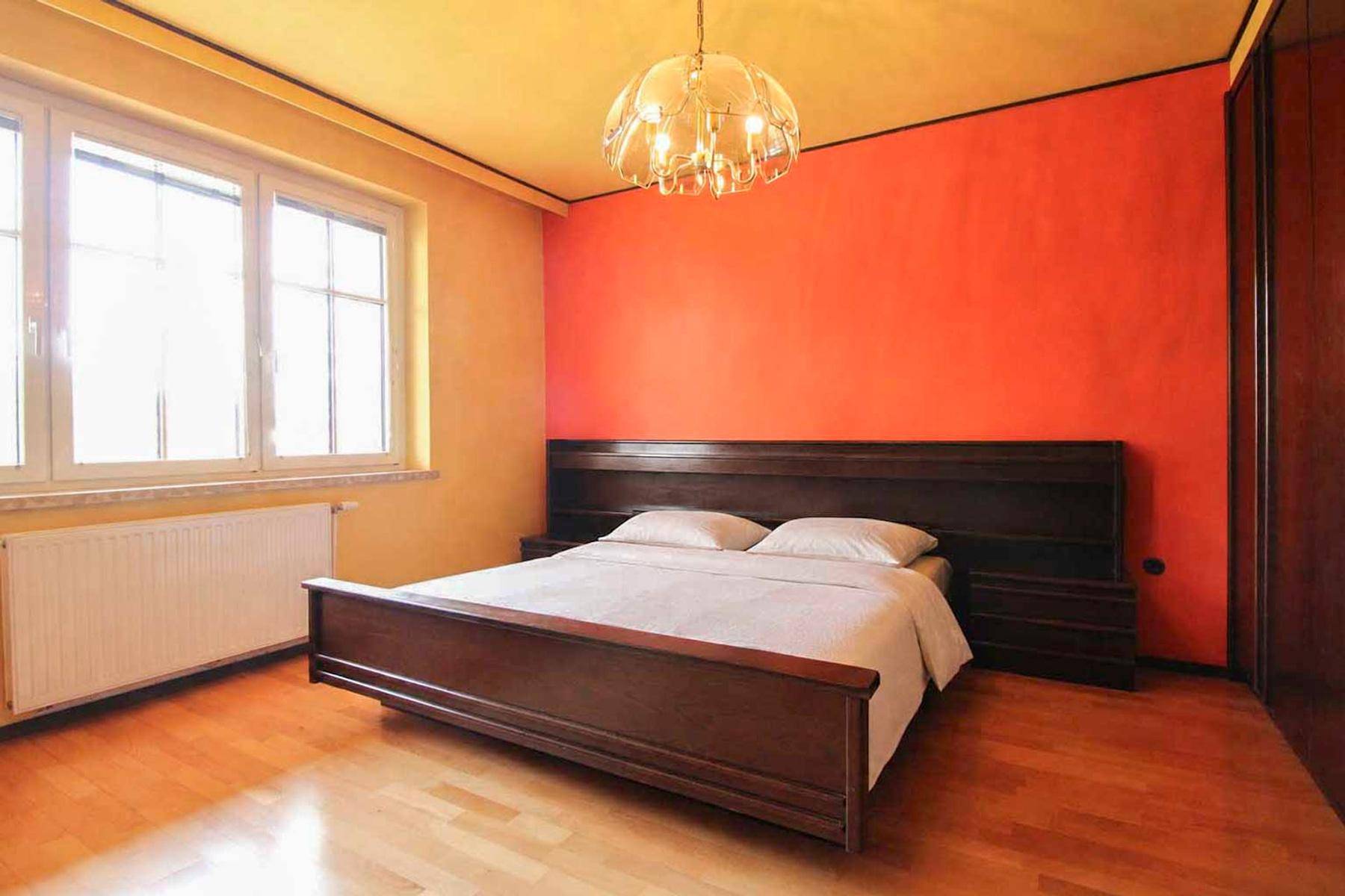 Schlafzimmer mit Holzbett, Parkettboden und einer auffälligen roten Akzentwand.