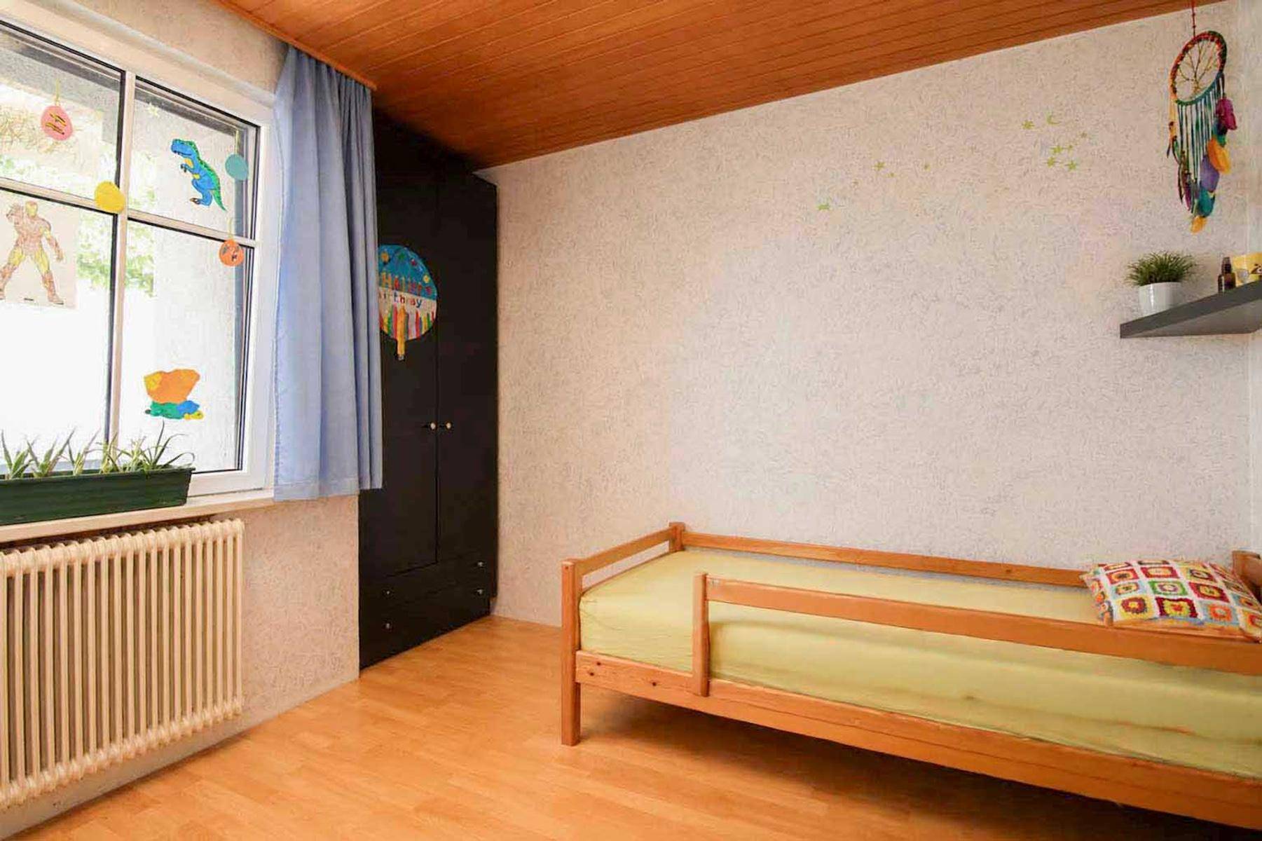 Kinderzimmer mit Holzdecke, Parkettboden und einem Einzelbett.