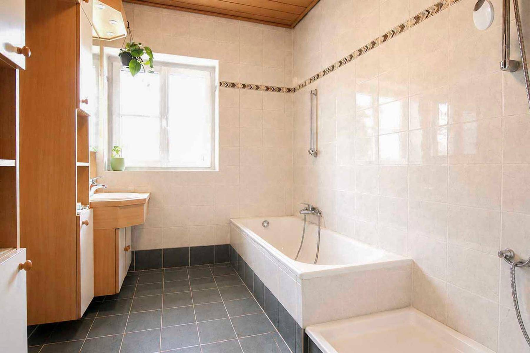 Klassisches Badezimmer mit Badewanne, Fenster und hellen Fliesen.