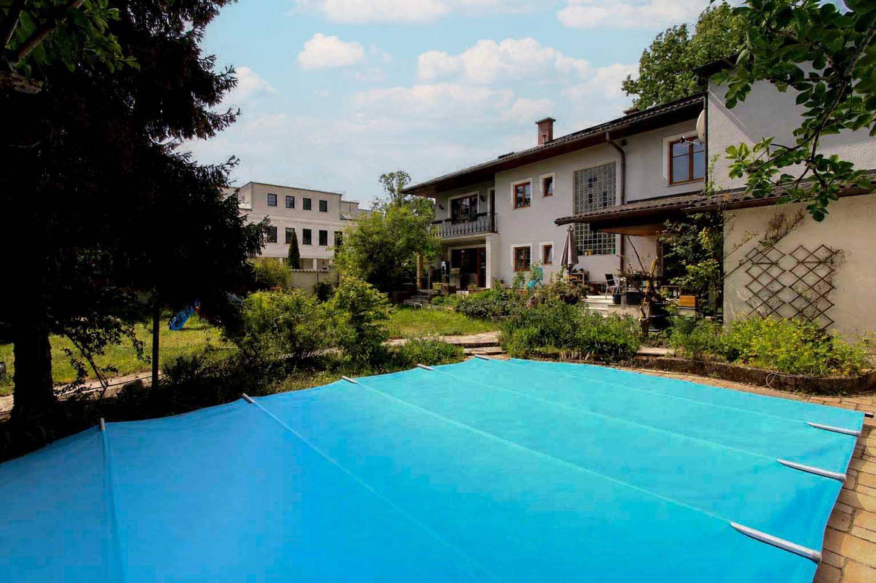 Großer Garten mit Rasenfläche, Bäumen und einem abgedeckten Pool.