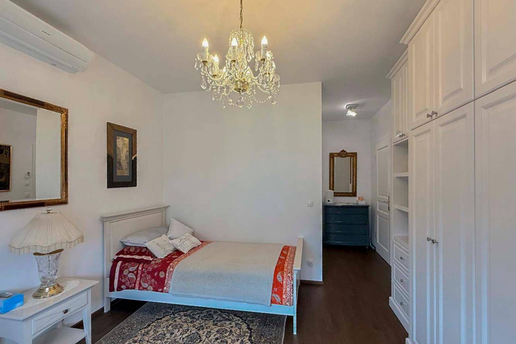 Helles Schlafzimmer mit Einzelbett, weißem Kleiderschrank und Kronleuchter.