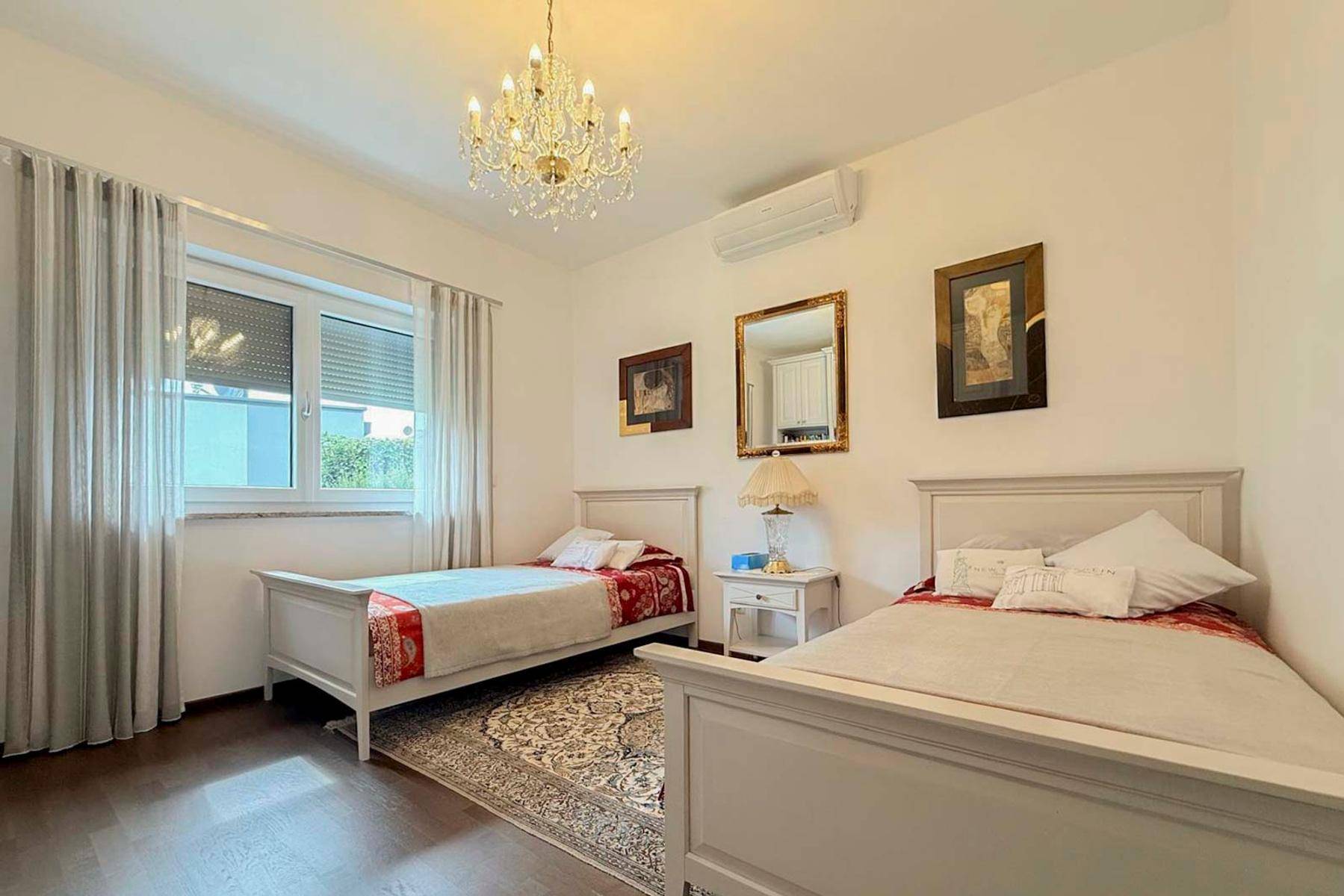 Schlafzimmer mit zwei Einzelbetten, Fenster und elegantem Kronleuchter.