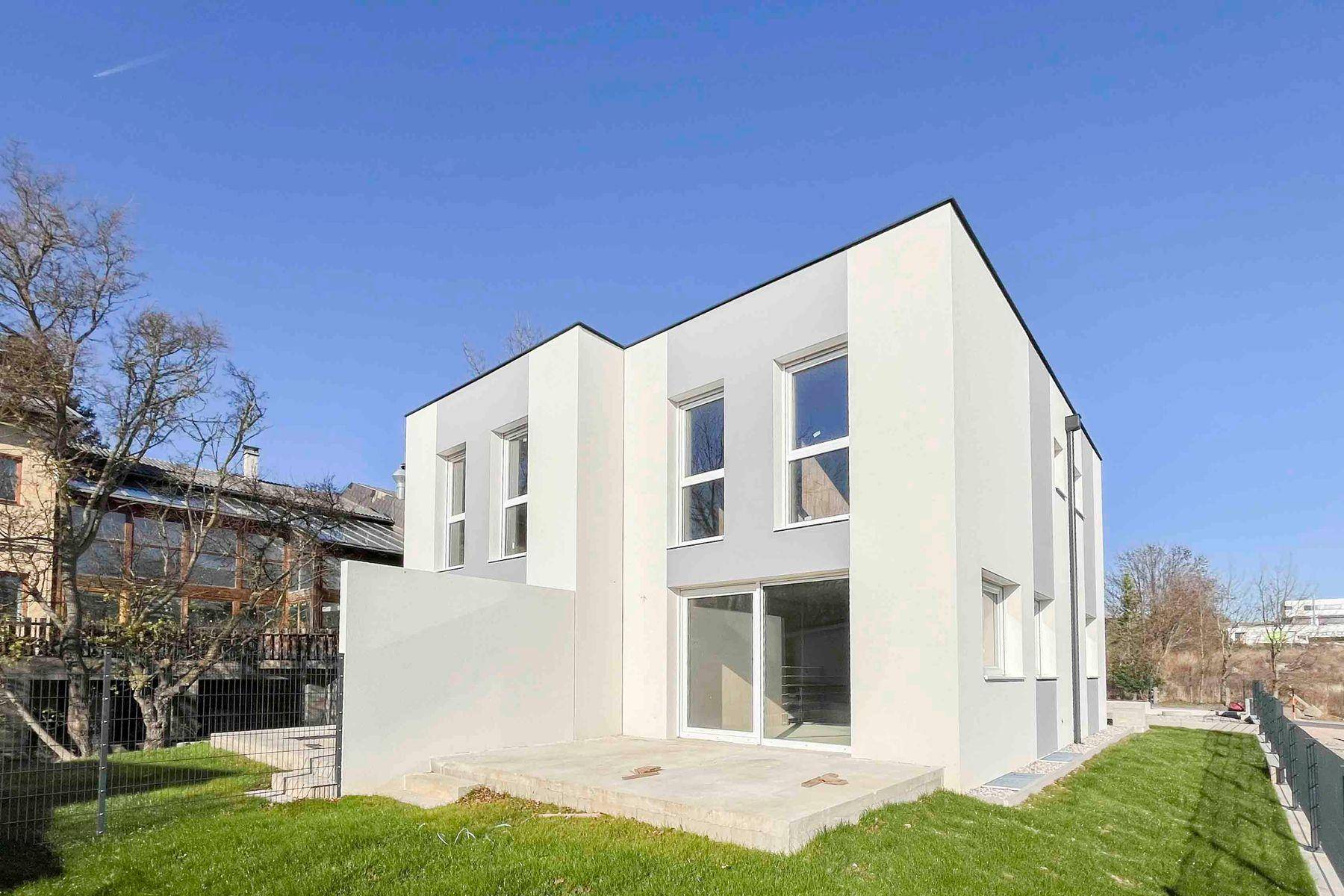 Ansicht des modernen Neubaus mit klaren Linien und einer kleinen Terrasse im Grünen.