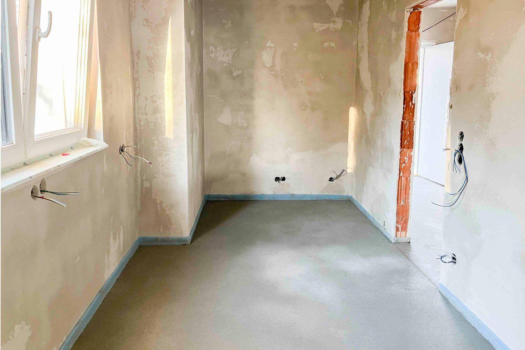 Unfertiger Innenraum mit Estrichboden und vorbereiteten Elektroinstallationen für den Ausbau.