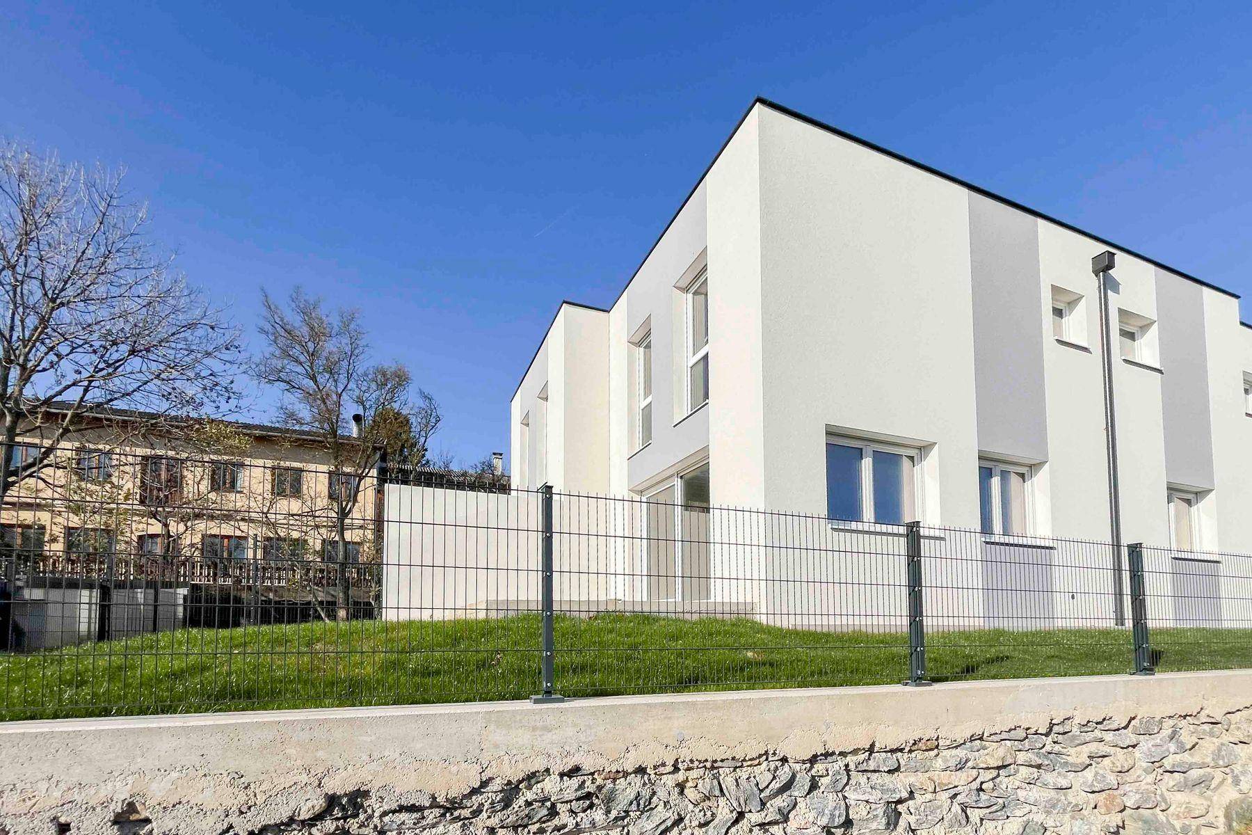 Frontansicht des modernen Neubaus mit weißer Fassade und umzäuntem Vorgartenbereich.