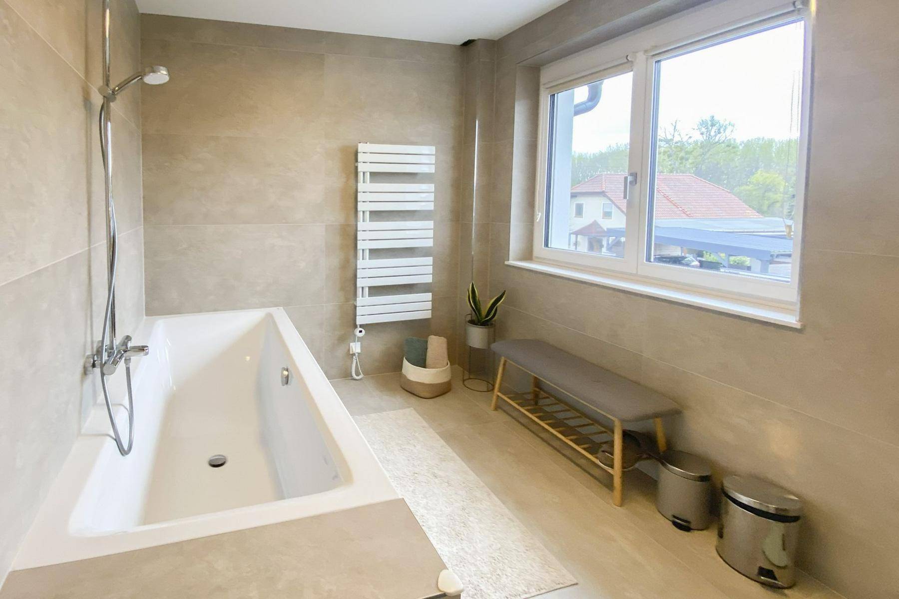 Helles Badezimmer mit Badewanne, Duschfunktion und beheiztem Handtuchhalter.