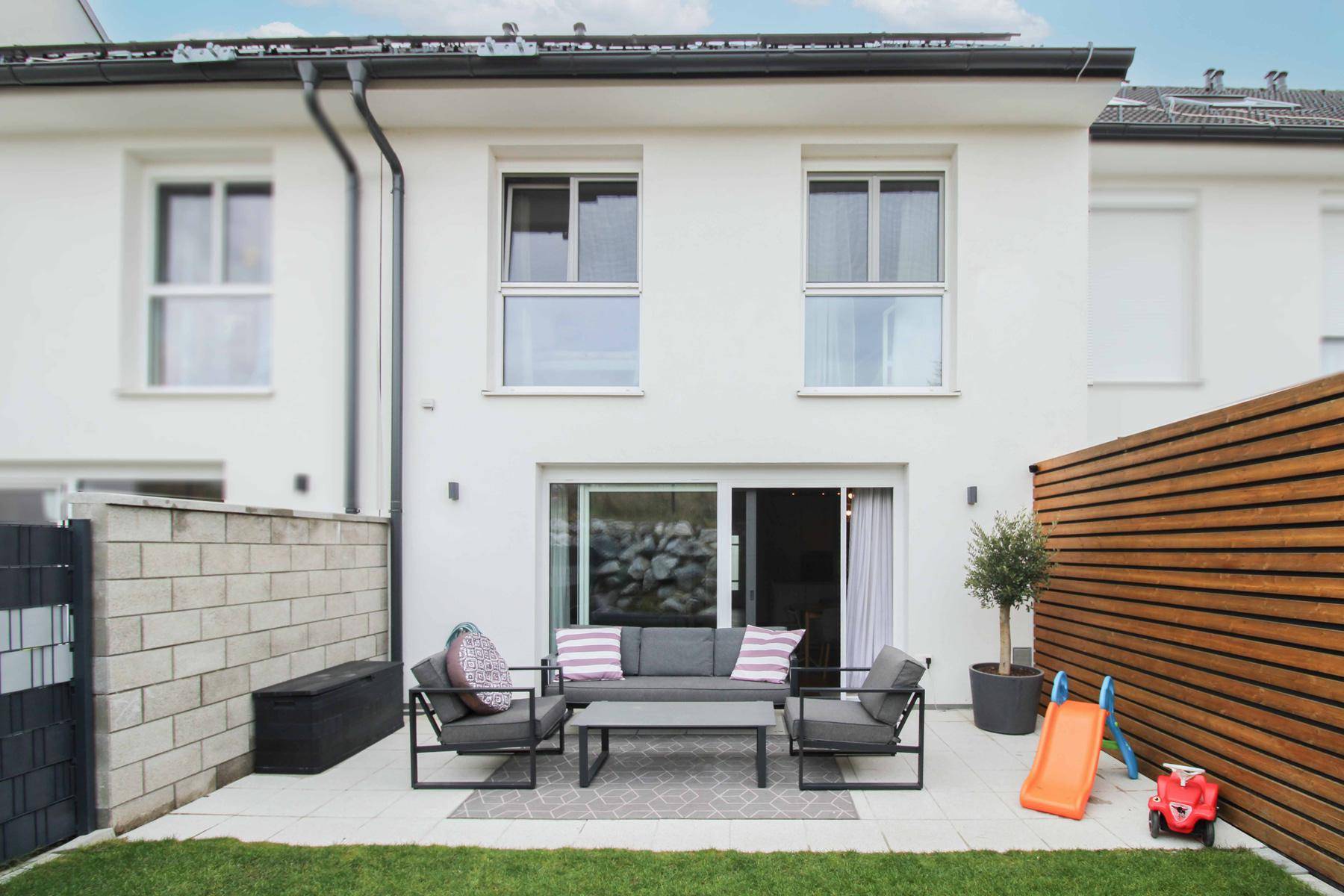 Moderne Terrasse mit Sitzgelegenheiten, kleinem Rasen und Zugang zum Garten.
