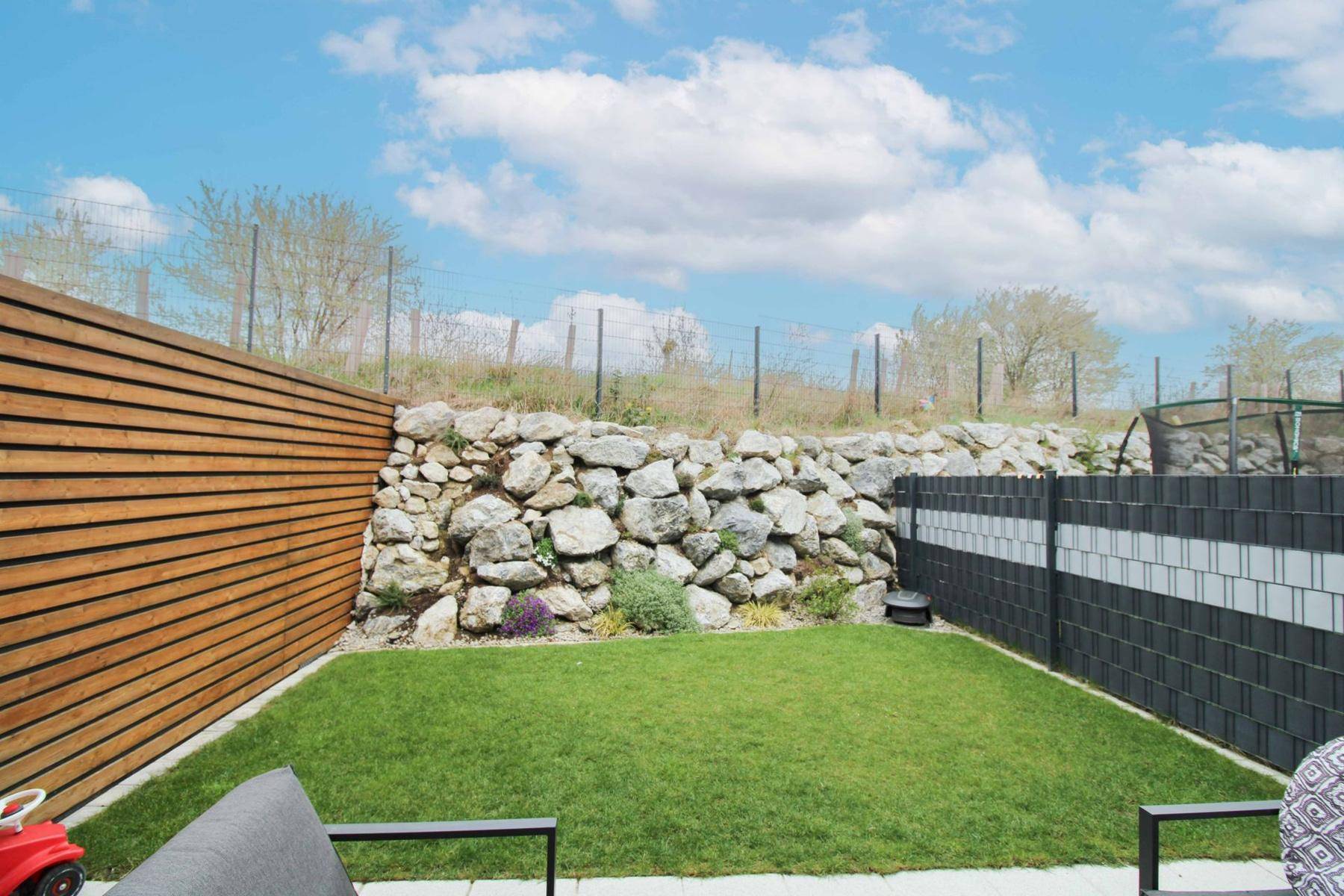 Kleiner, gepflegter Gartenbereich mit Rasenfläche, Steinmauer und Holzzaun.