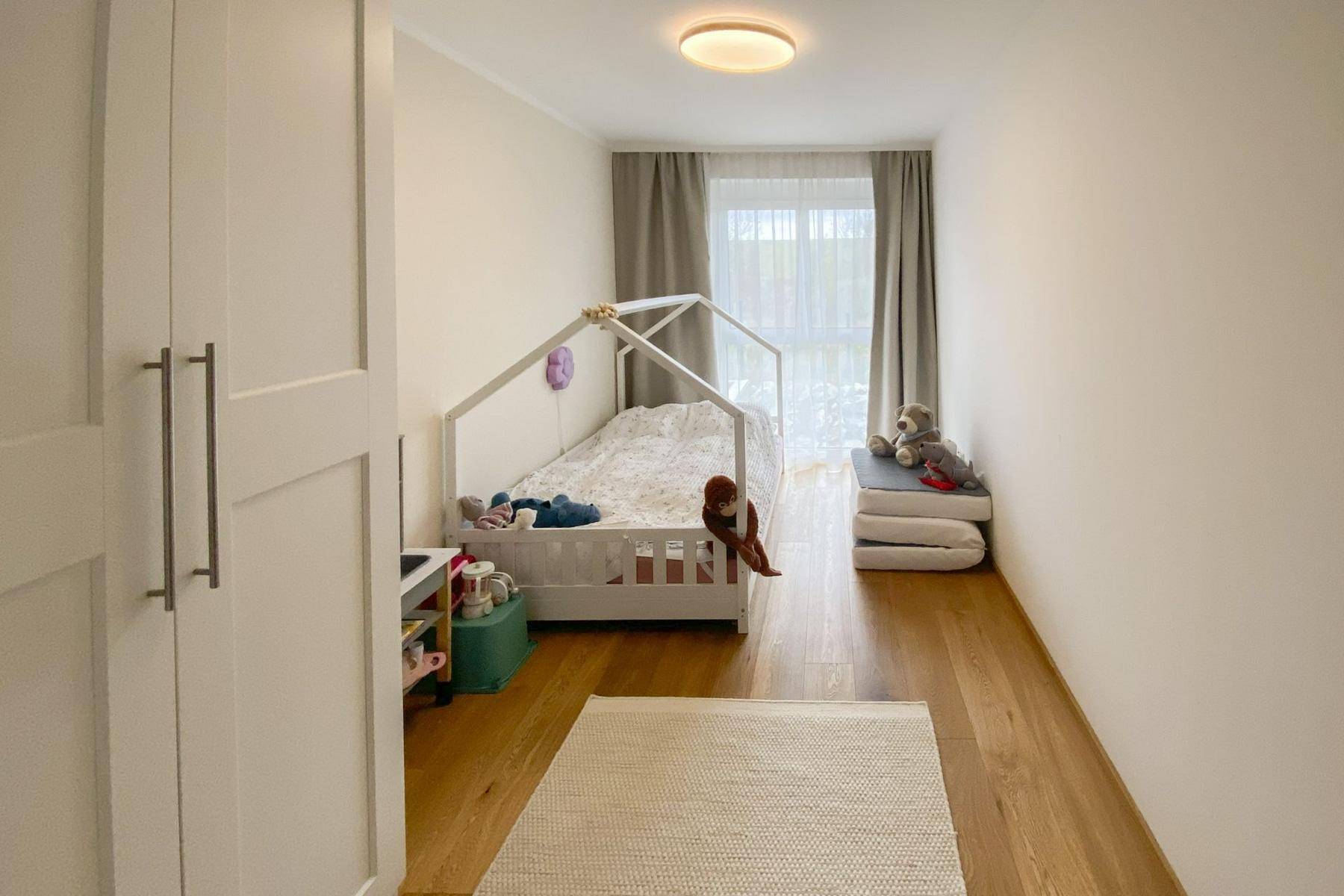 Kinderzimmer mit Hausbett, weißem Kleiderschrank und hellem Holzboden.