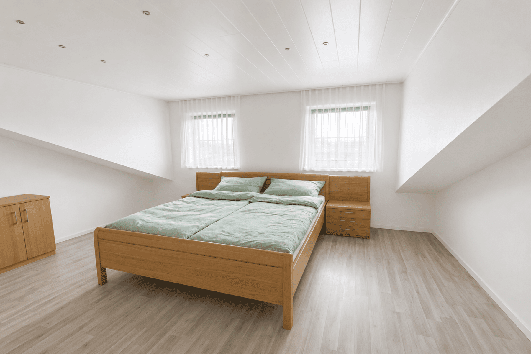 Geräumiges Schlafzimmer mit Holzdoppelbett, Nachttischen und hellen Wänden unter Dachschrägen.