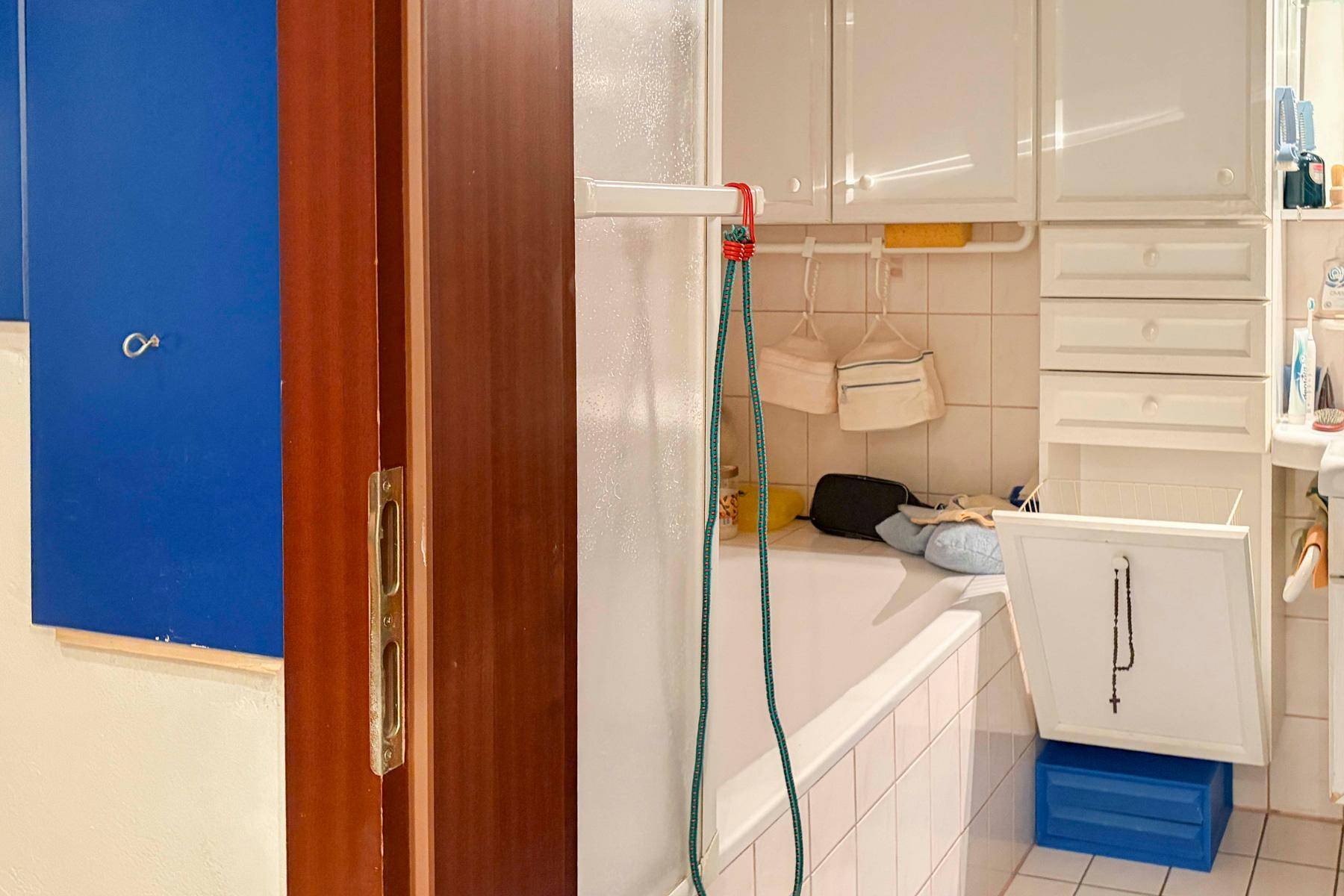 Badezimmer mit Badewanne, weißen Schränken und blauer Wand.