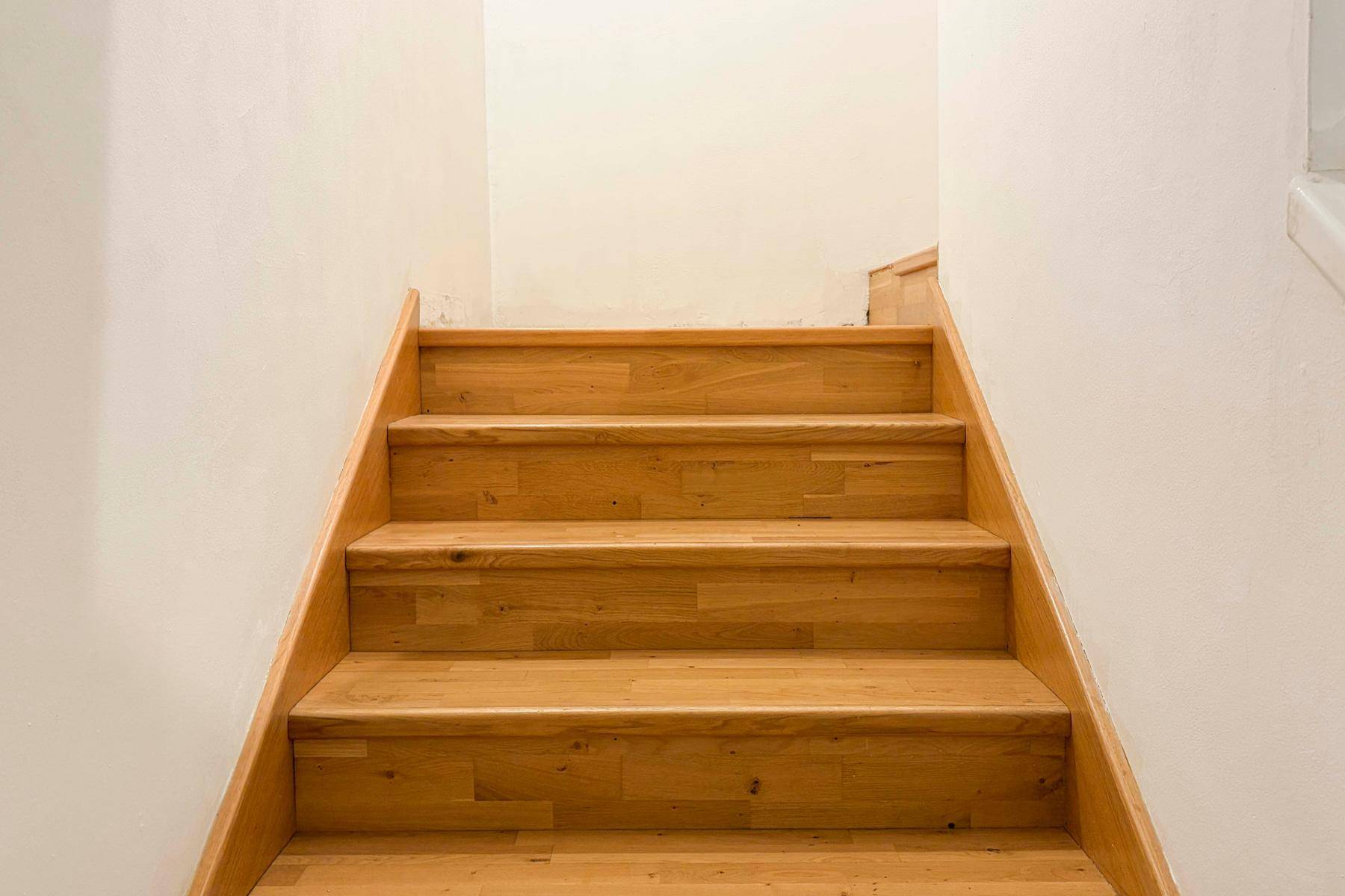 Helle Holztreppe mit weißen Wänden, die in ein oberes Stockwerk führt.