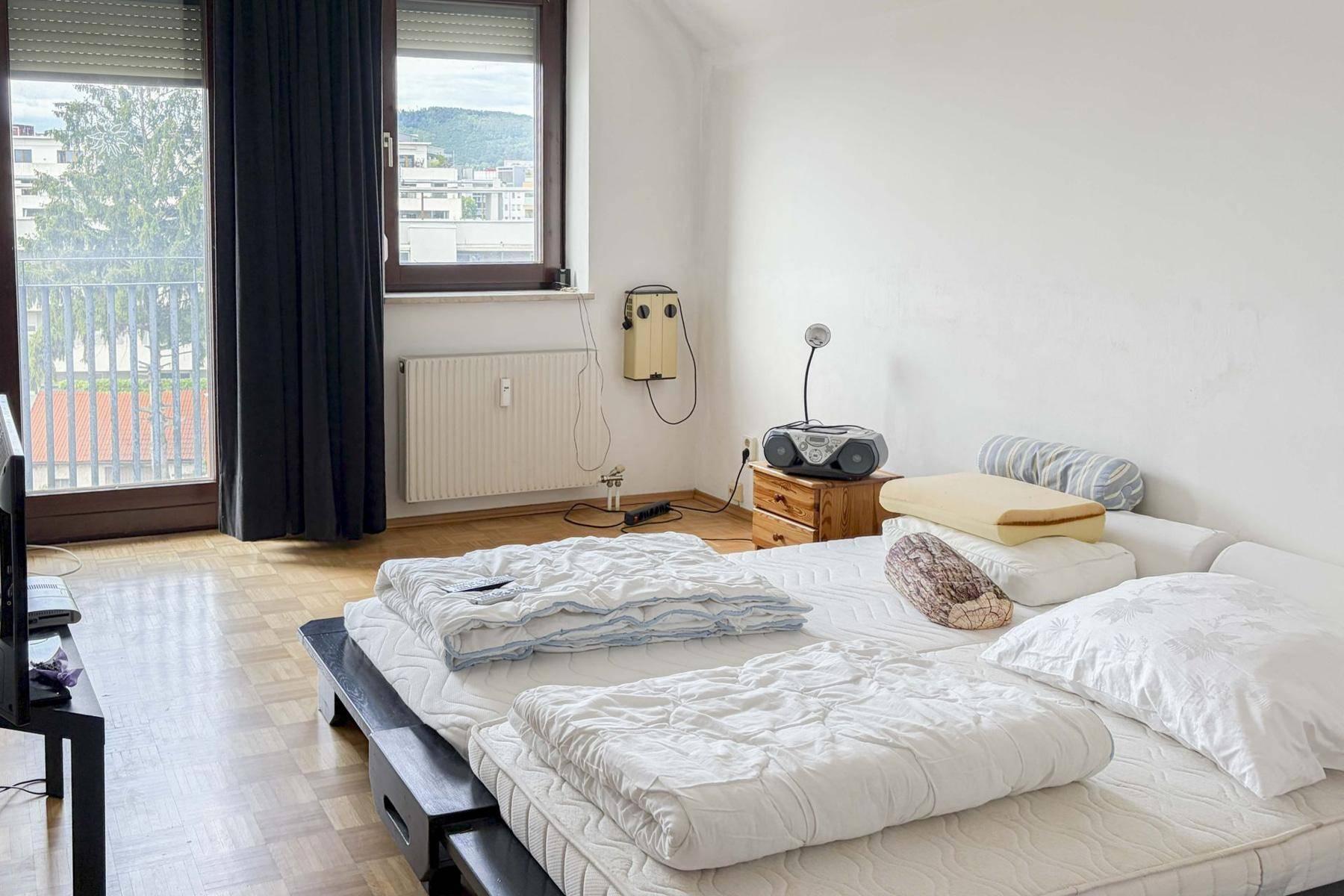 Helles Schlafzimmer mit zwei Betten, Parkettboden und Zugang zu einem Balkon.
