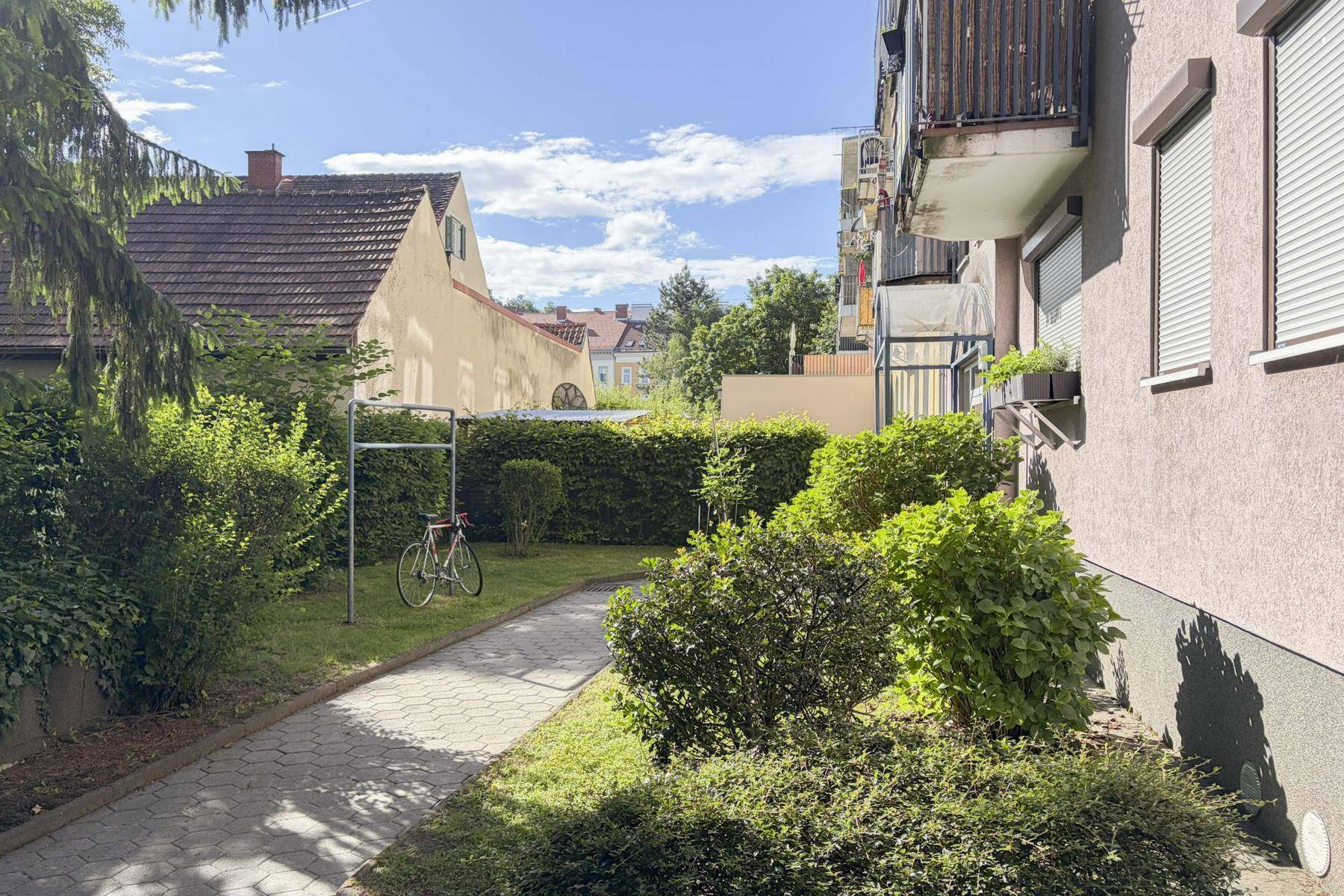 Gepflegter Gartenbereich mit Hecken, Rasen und einem gepflasterten Weg.