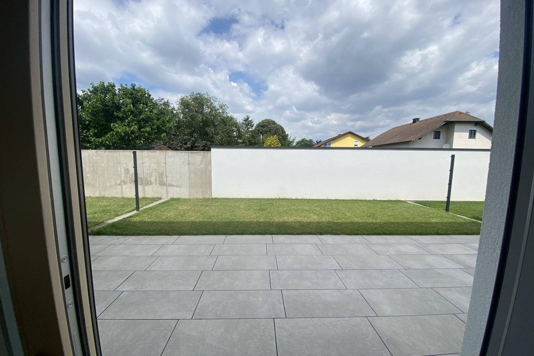 Blick vom Innenraum auf die gepflasterte Terrasse und den grünen Garten.