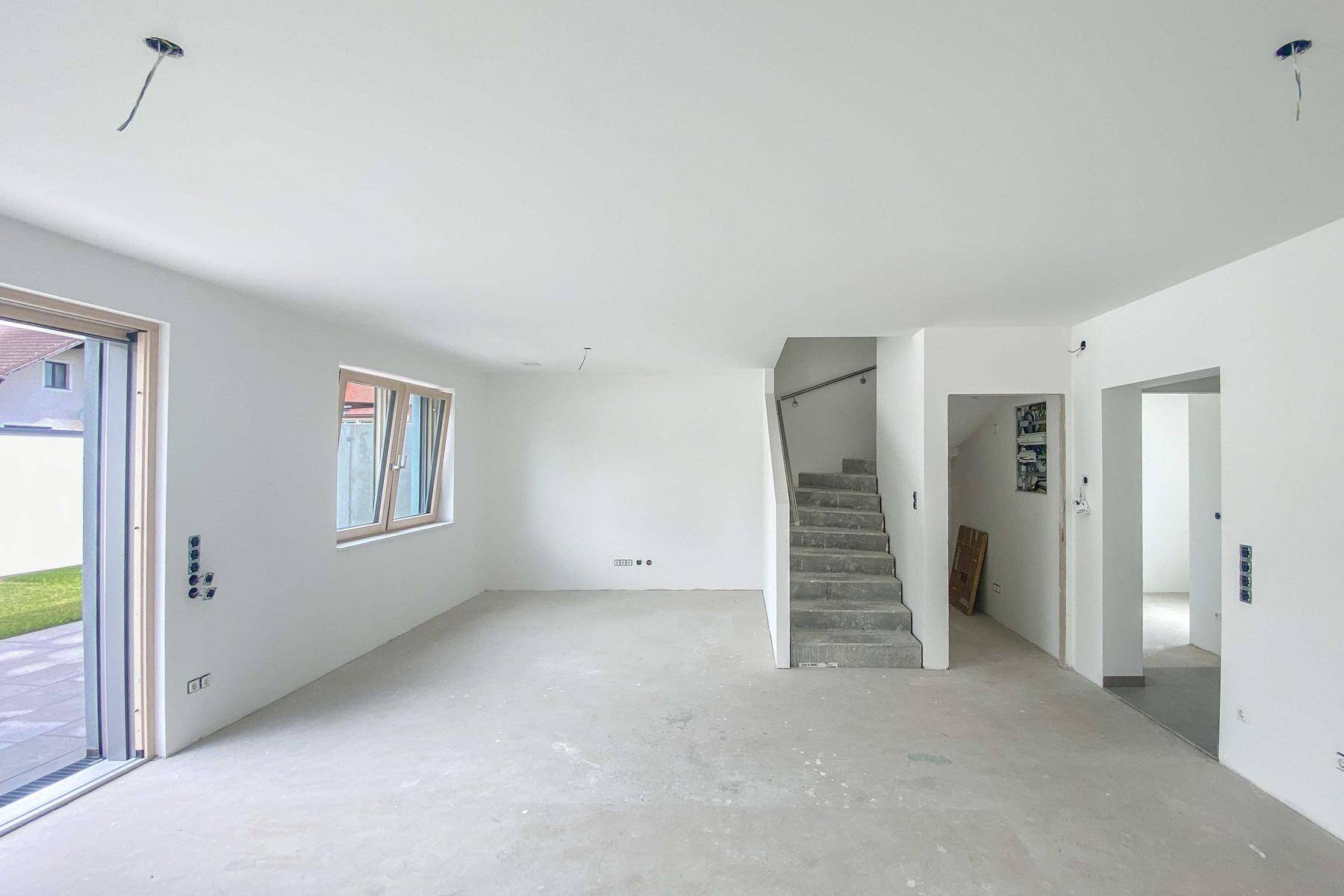 Heller Wohnbereich mit Zugang zum Garten und offener Treppe zum Obergeschoss.