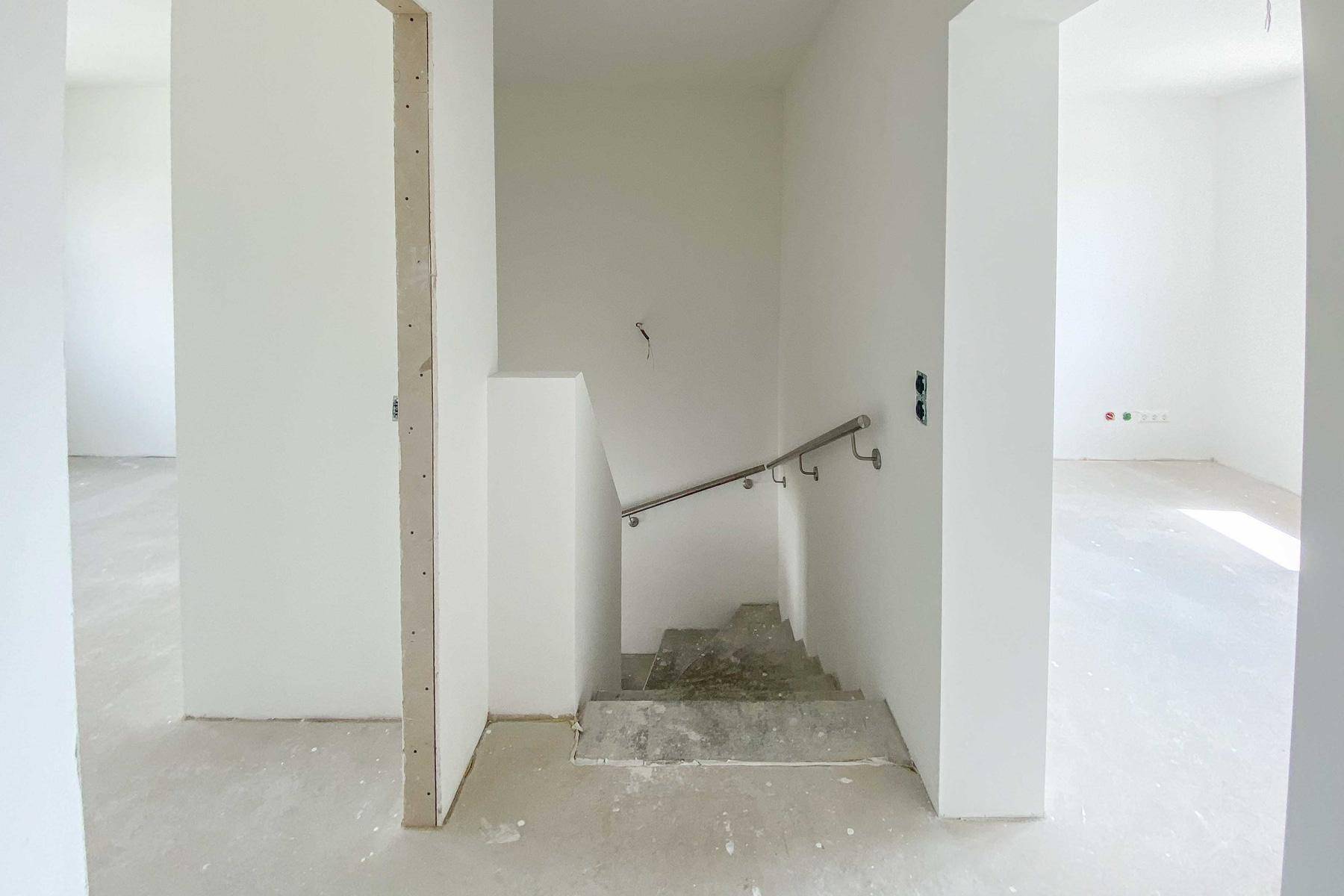 Treppenaufgang mit Geländer in einem hellen, unfertigen Innenbereich des Neubaus.
