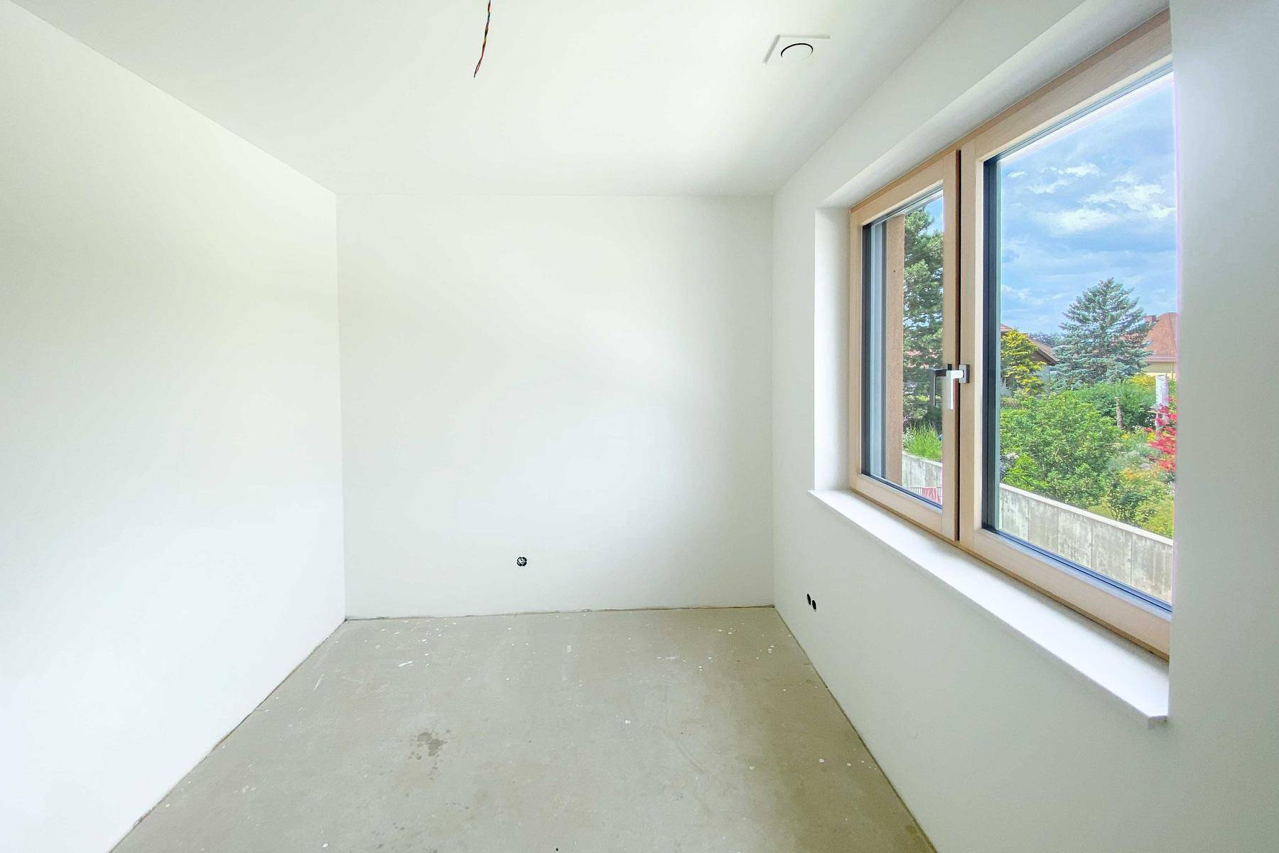 Leerer, unmöblierter Raum in einem Neubau mit großem Fenster und Blick ins Grüne.