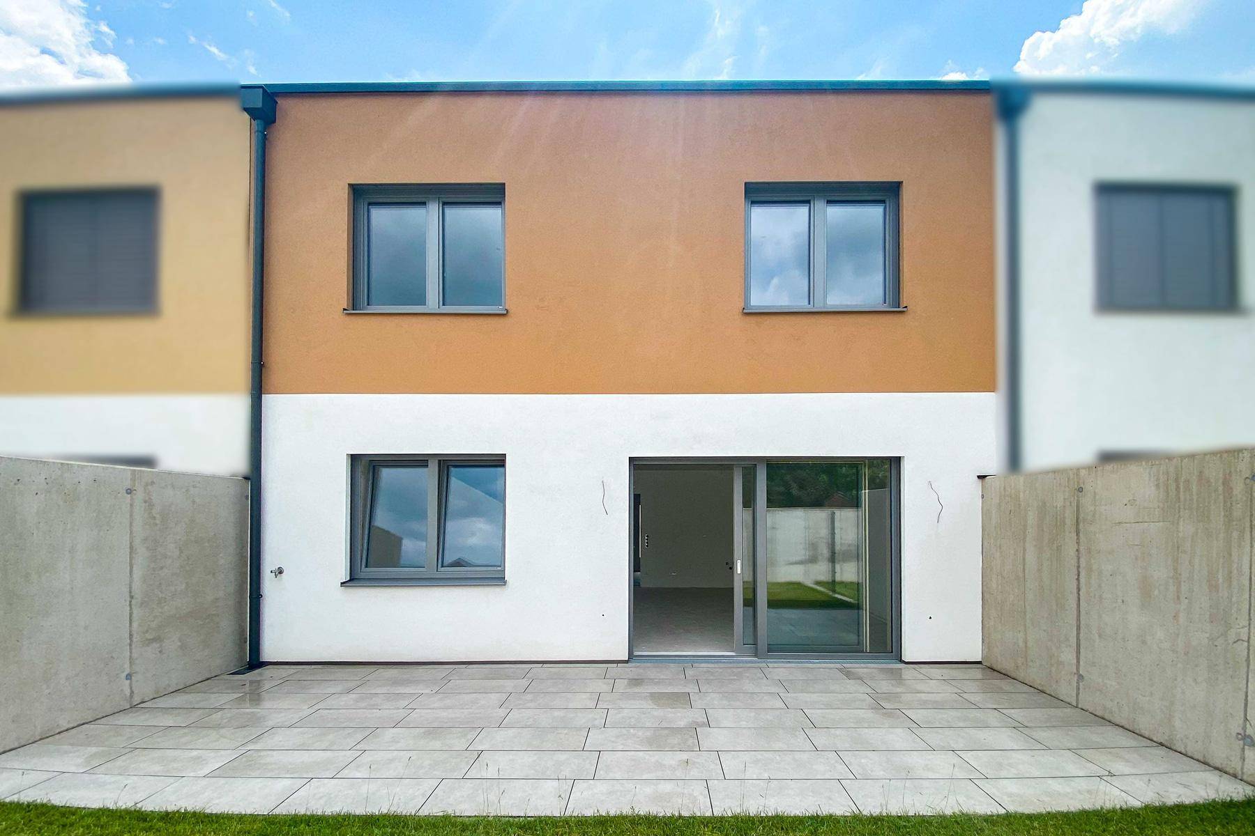 Rückseite eines Reihenhauses mit gepflasterter Terrasse und kleinem Rasenbereich.