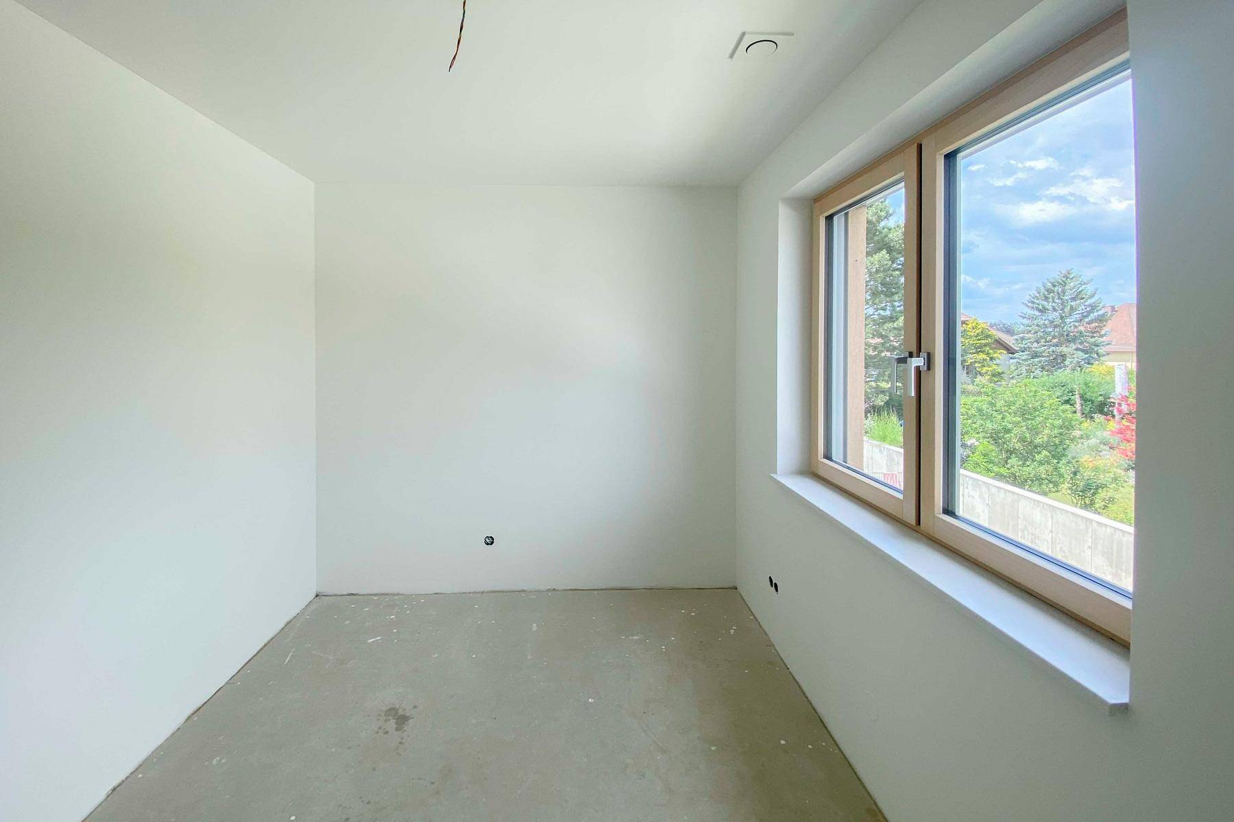 Helles, unfertiges Schlafzimmer mit Fenster und Blick ins Grüne.