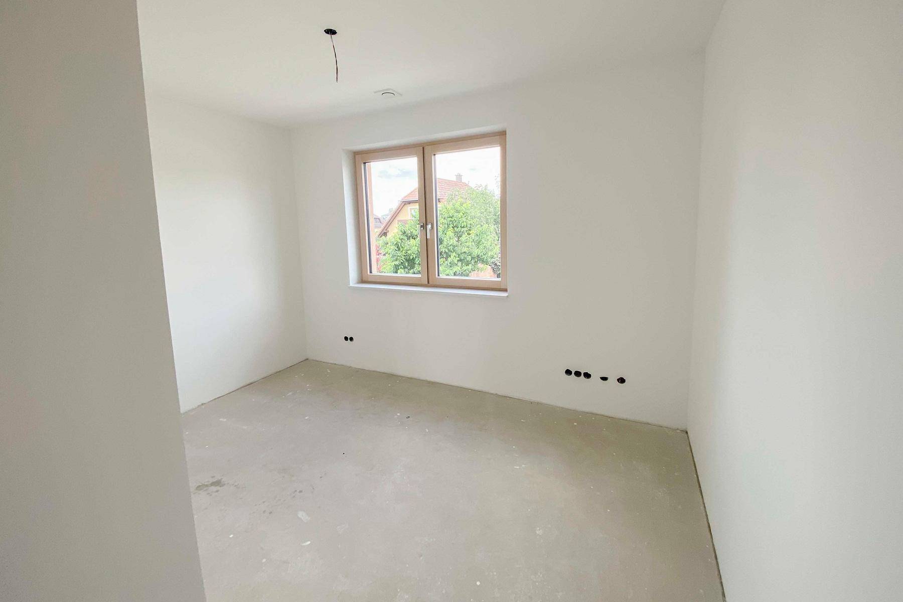 Helles, unfertiges Schlafzimmer mit Fenster und Blick auf die grüne Umgebung.