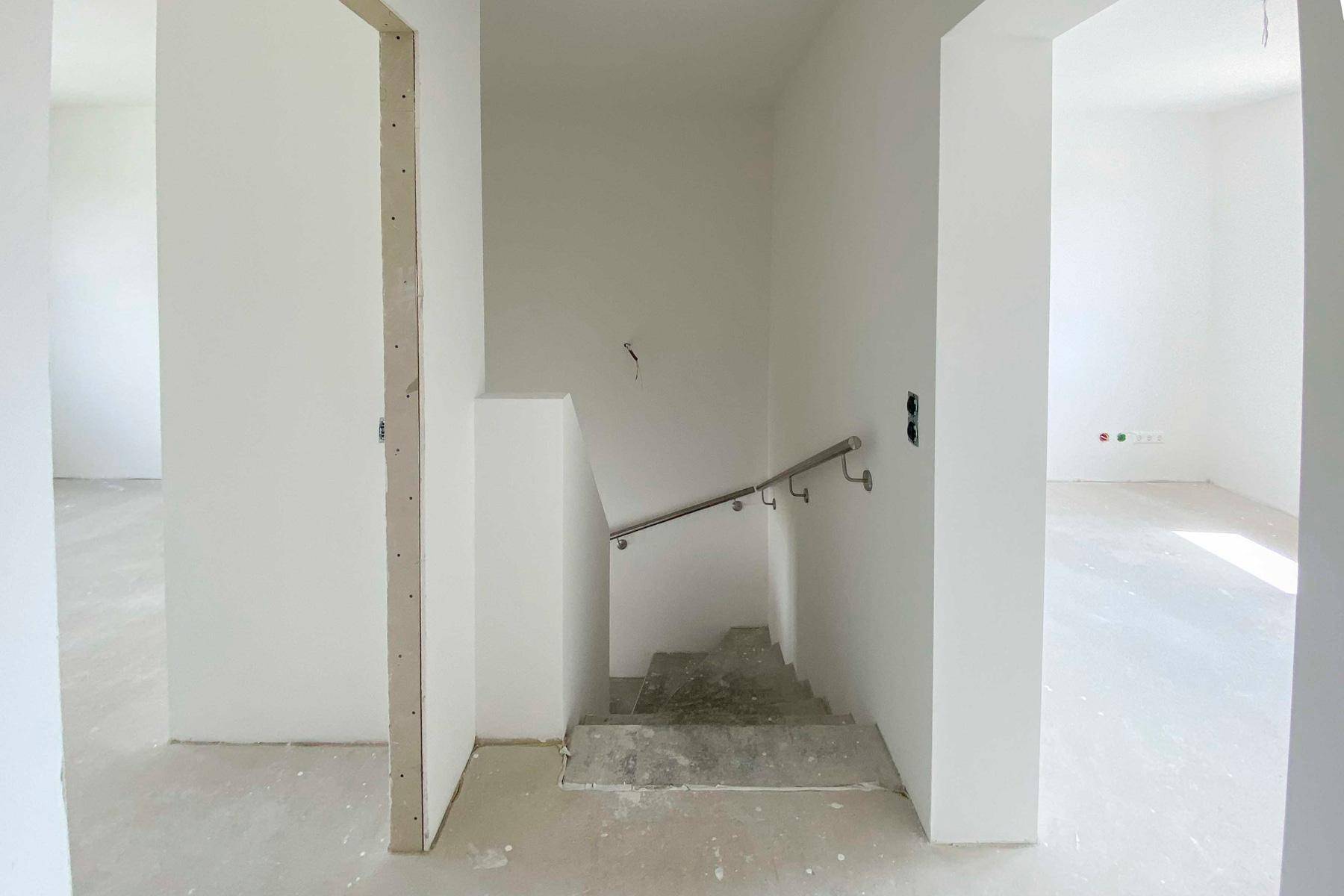 Unfertiger Treppenaufgang mit Handlauf, der in die obere Etage führt.