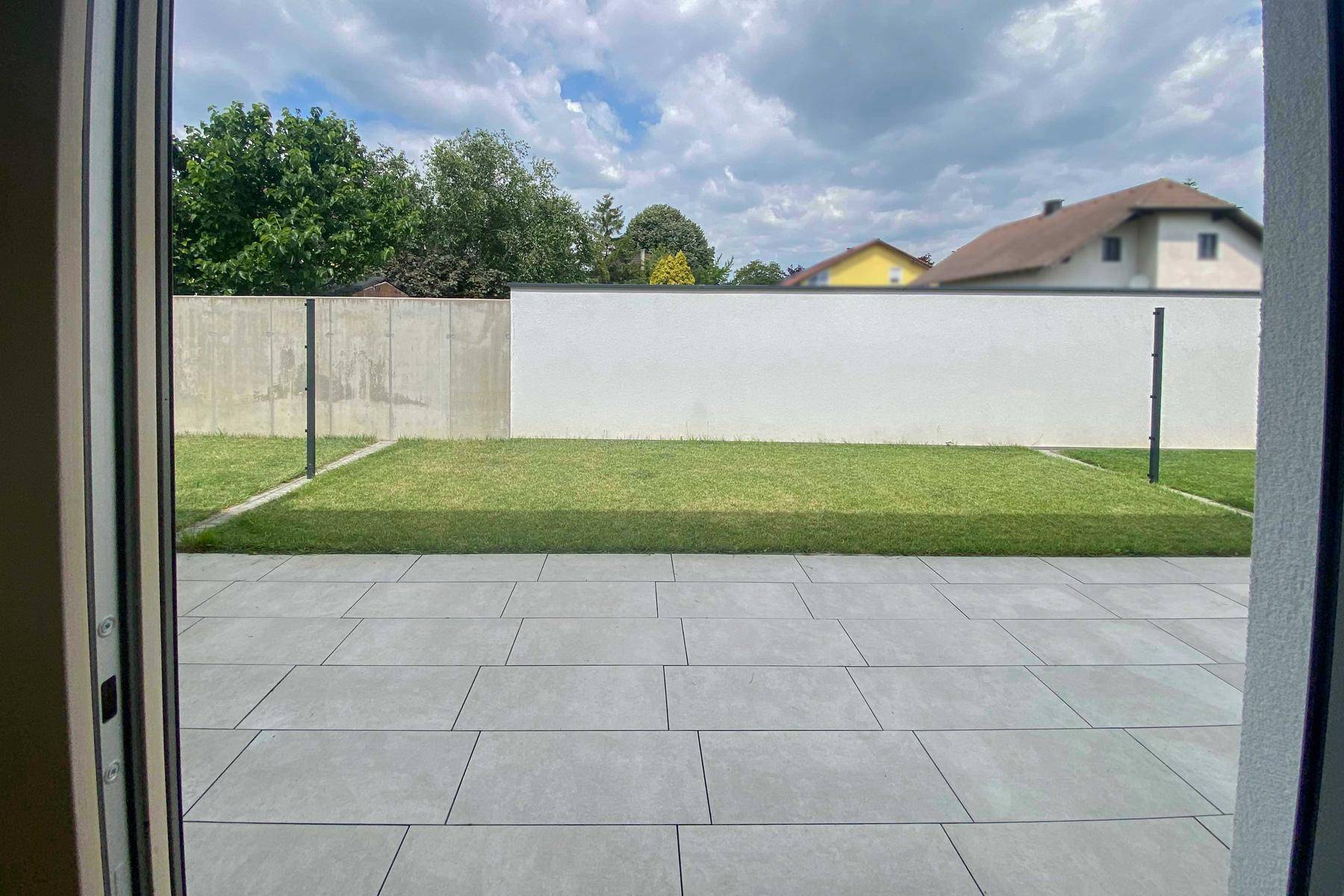 Blick von innen auf die gepflasterte Terrasse und den kleinen Gartenbereich.
