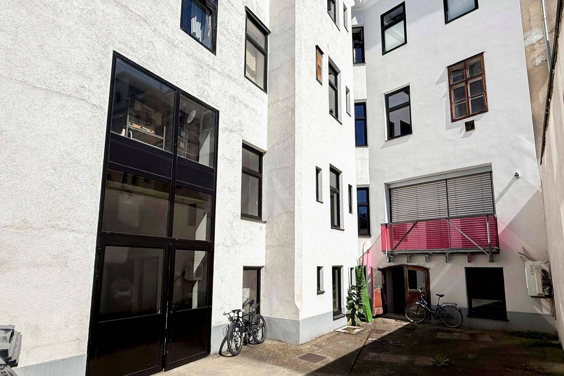 Heller Innenhof eines Gebäudes mit vielen Fenstern und abgestellten Fahrrädern, der Tageslicht spendet.