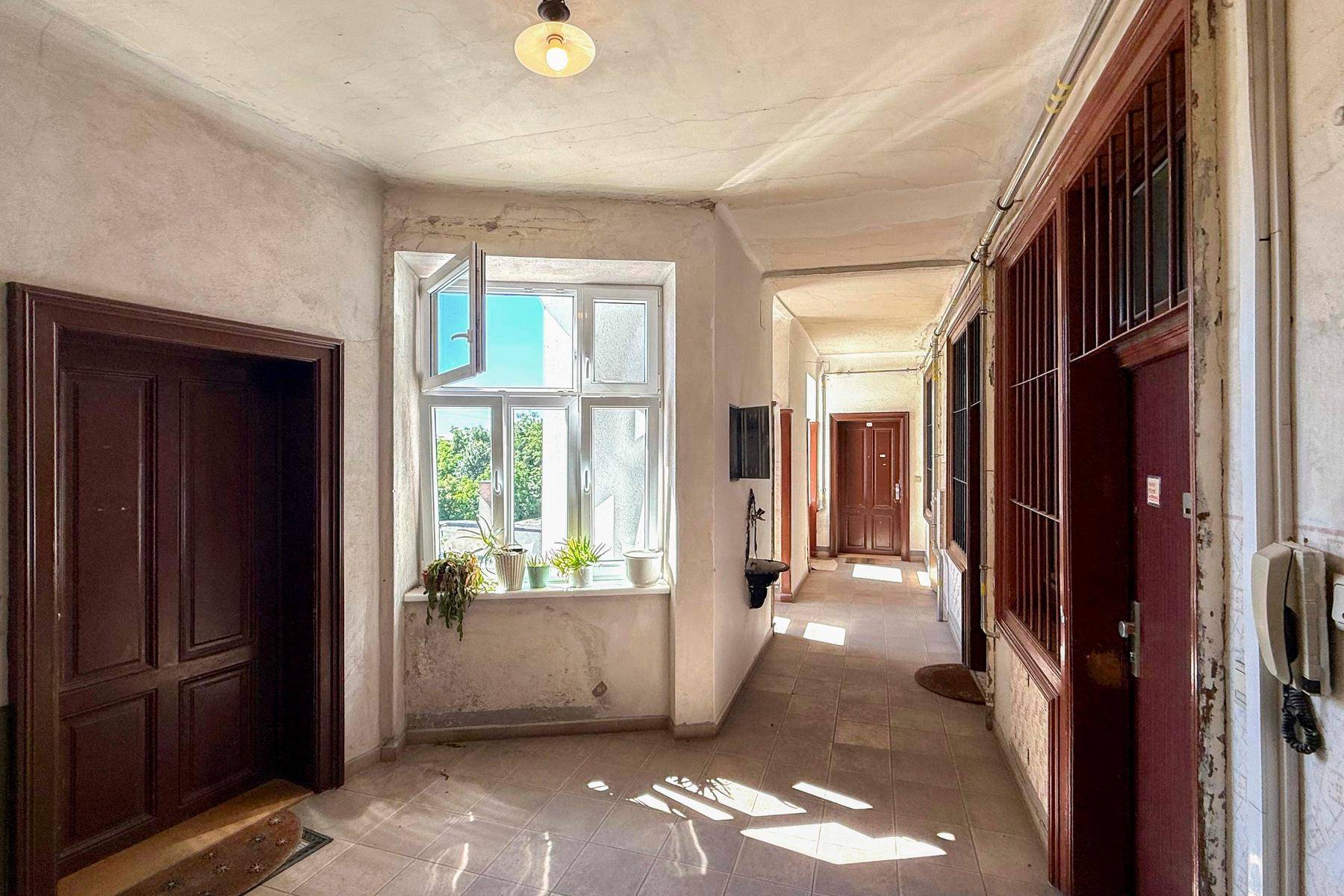 Langer Flur in einem Altbau mit Fliesenboden, mehreren Holztüren und einem Fenster, das Tageslicht hereinlässt.