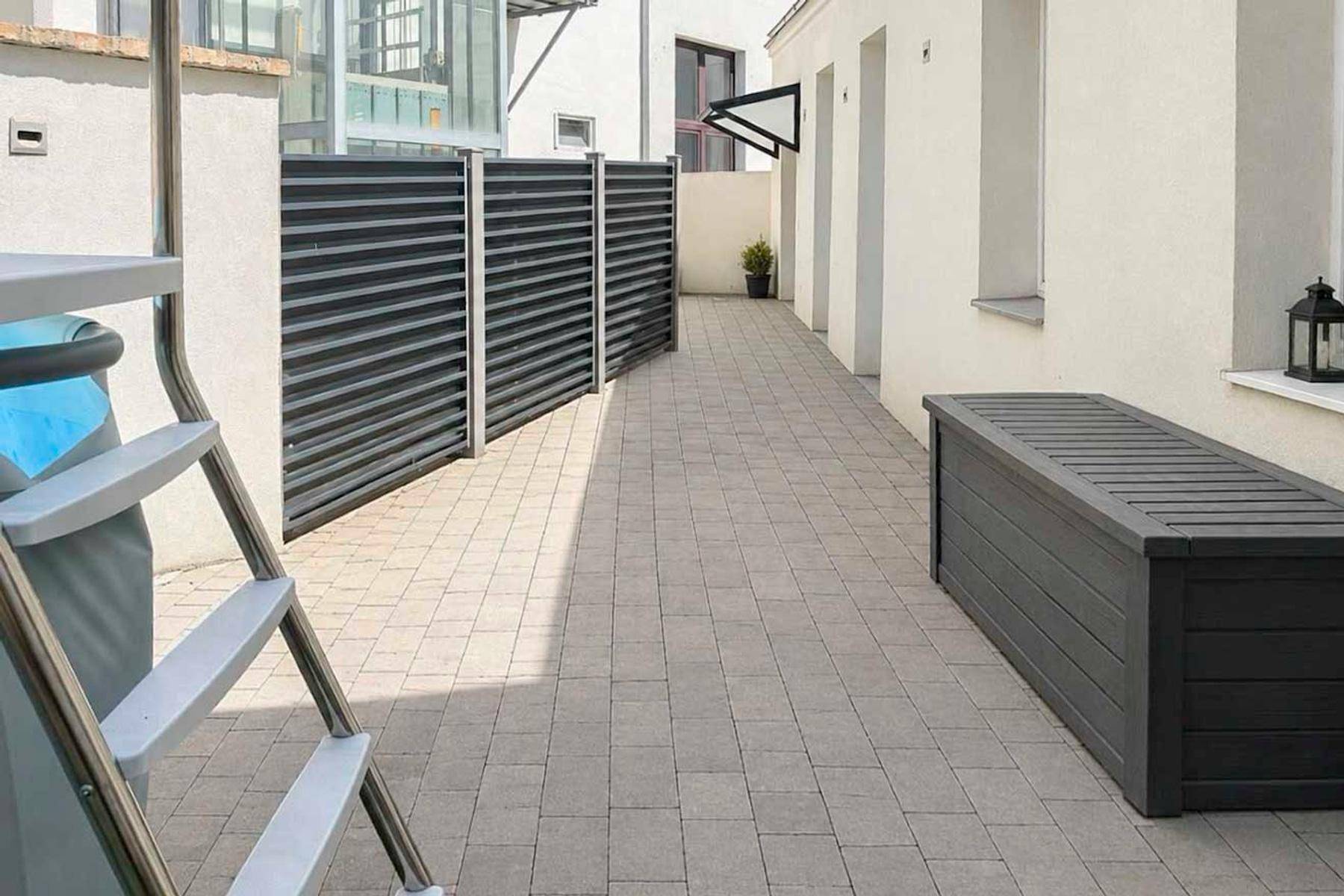 Außenbereich mit Pflastersteinen, Sichtschutzzaun und einer großen Aufbewahrungsbox, ideal für Freizeitaktivitäten.