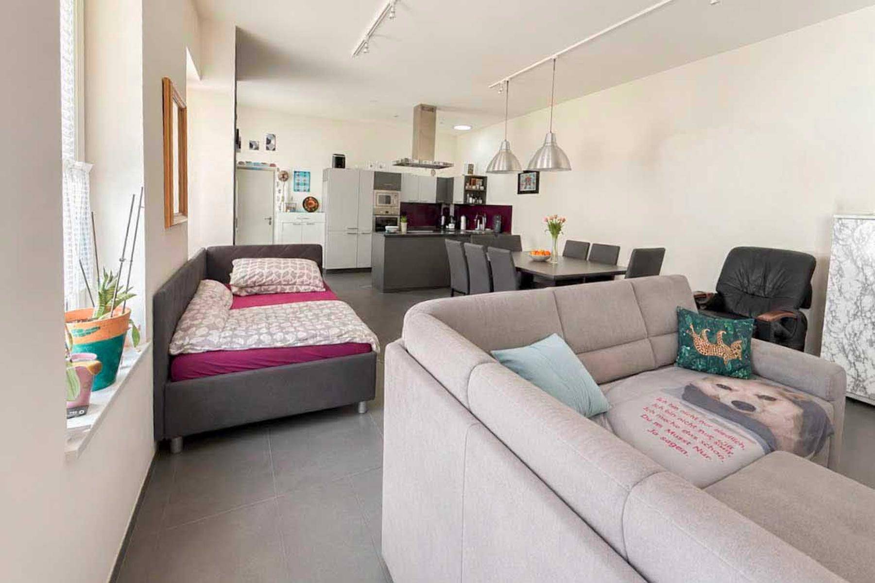 Heller, offener Wohnbereich mit Sofa, Tagesbett und Blick auf die moderne Küche und den Essbereich.
