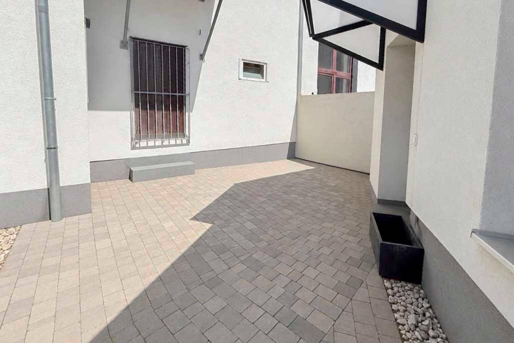 Gepflasterter Außenbereich zwischen Gebäuden mit einer Metalltür und sauberer, moderner Architektur.